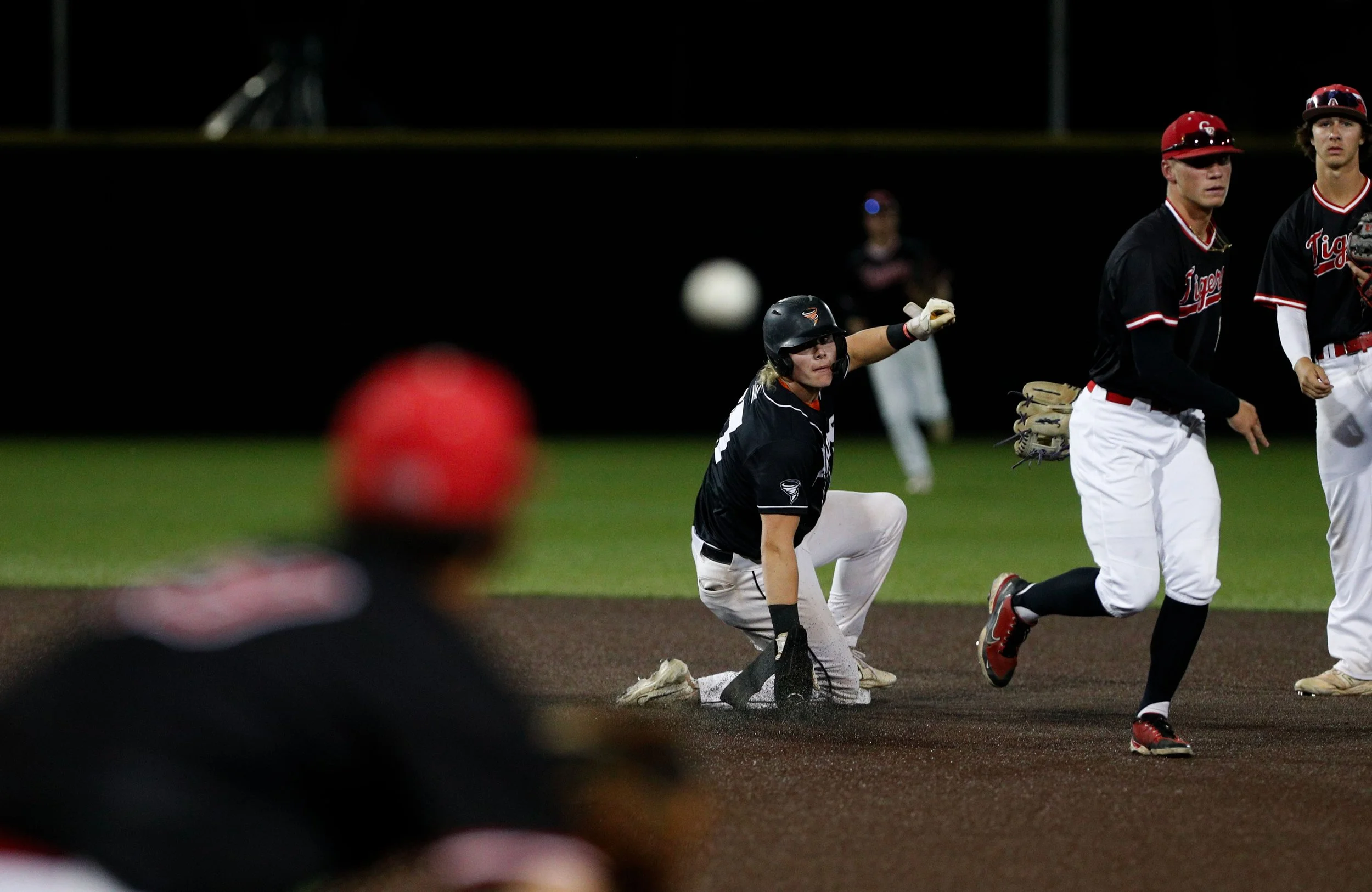 Baseball game scene showing players running and a player sliding into a base, with other players and a baseball visible.