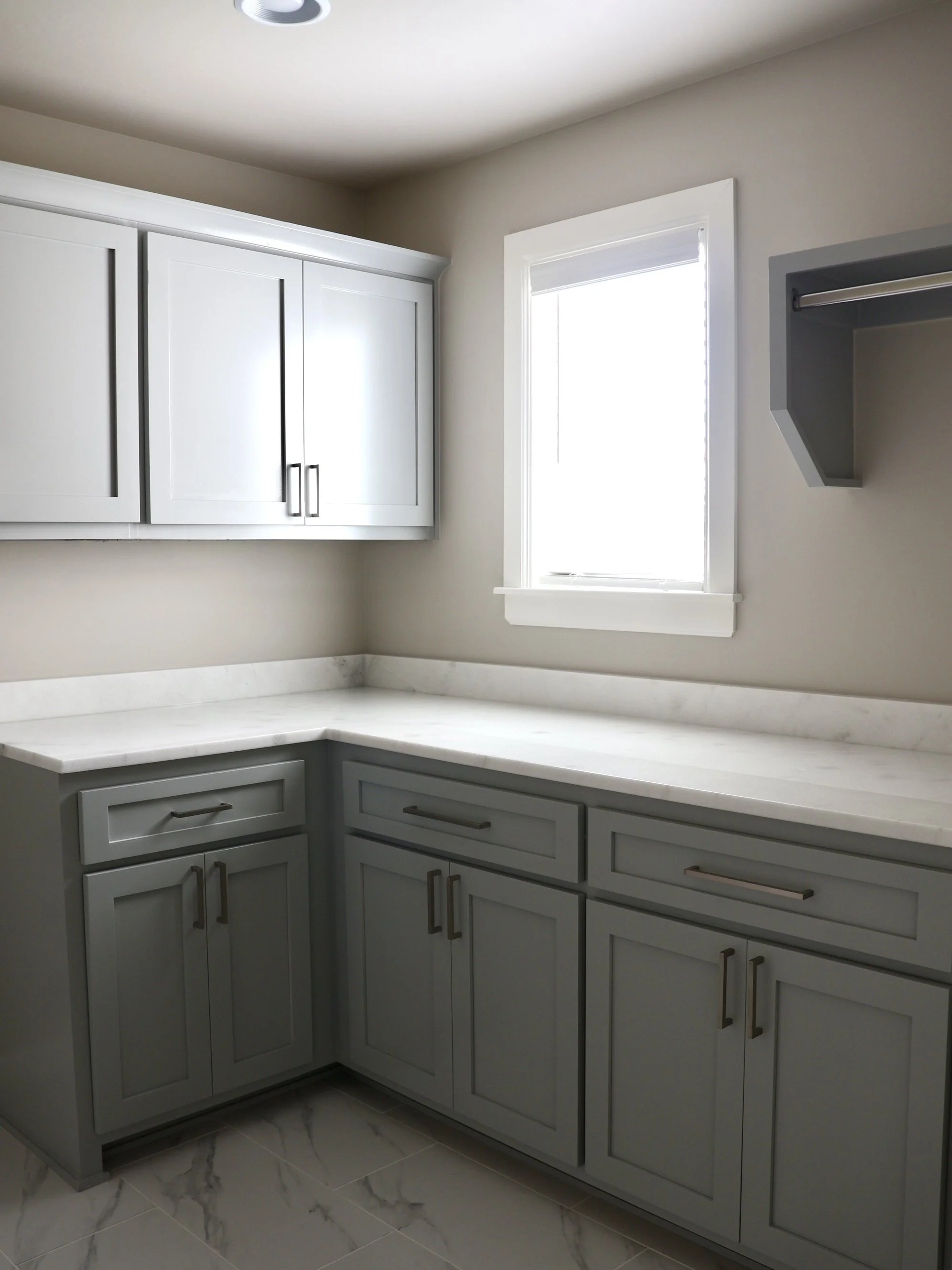 Kitchen with white cabinets, marble countertops, and a window with white trim.