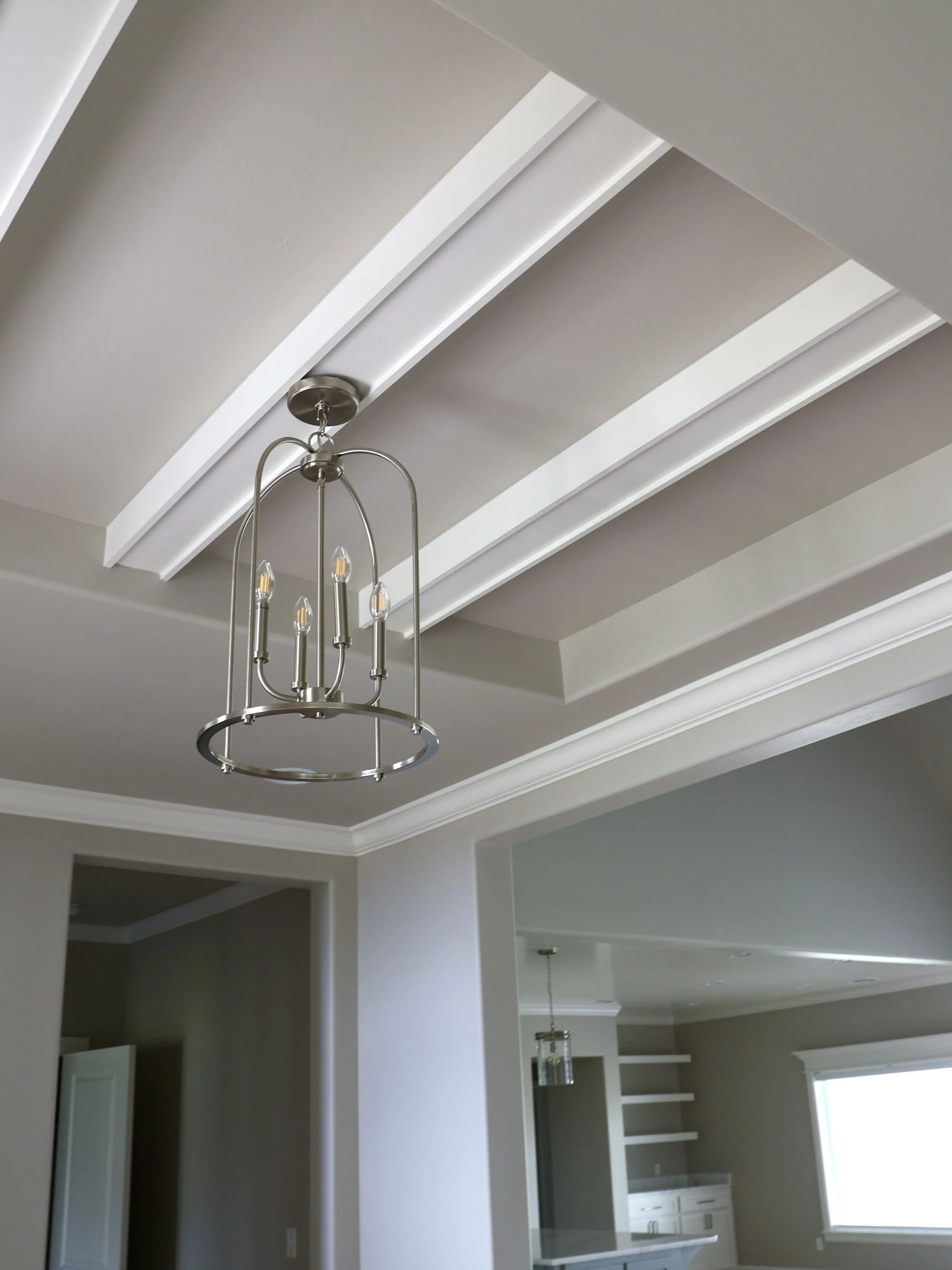 Interior view of a modern dining area with a ceiling featuring decorative molding and a metallic chandelier hanging from the ceiling.