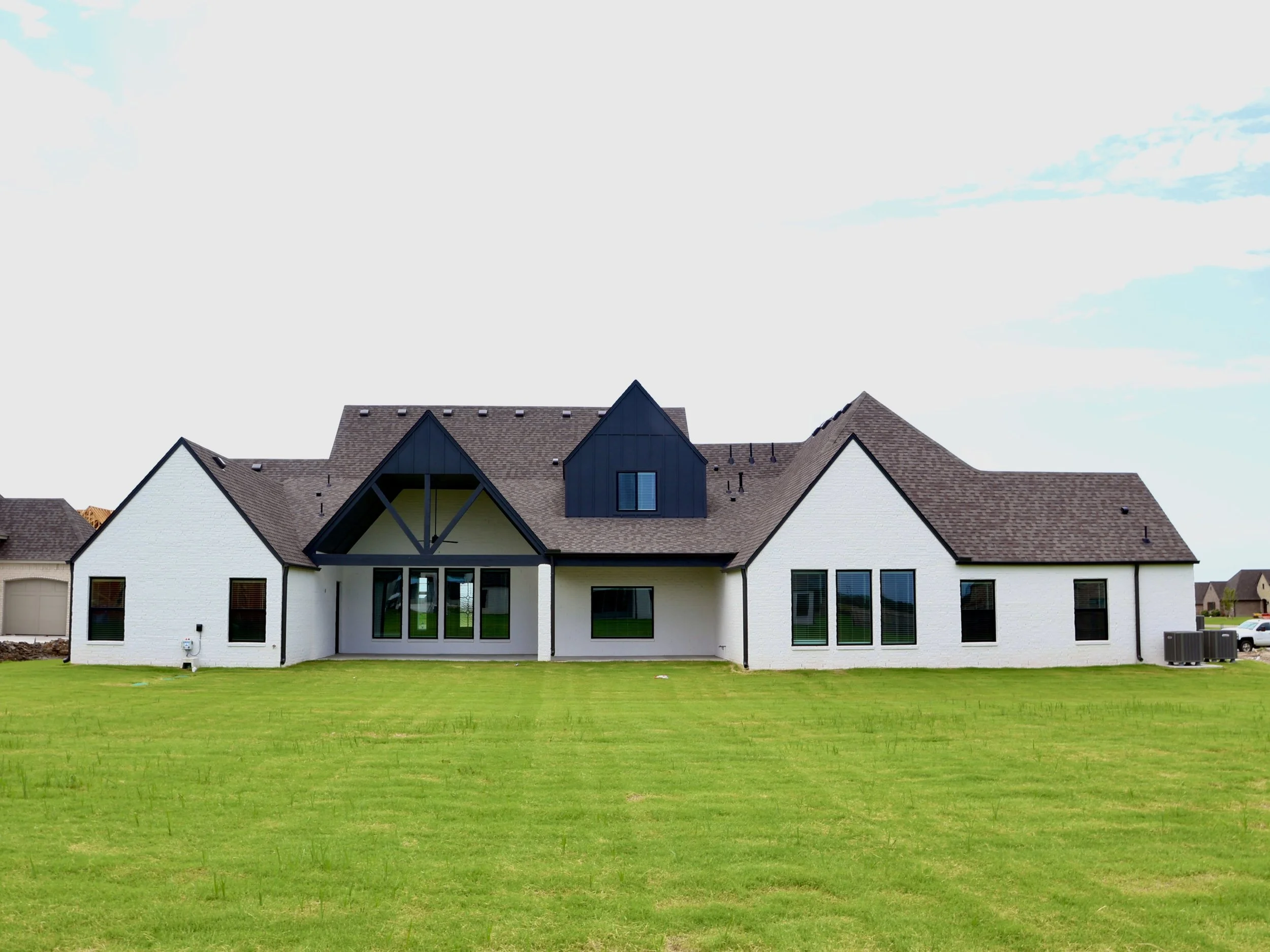 Modern house with white walls, black window frames, and a brown shingled roof, situated on a green lawn.