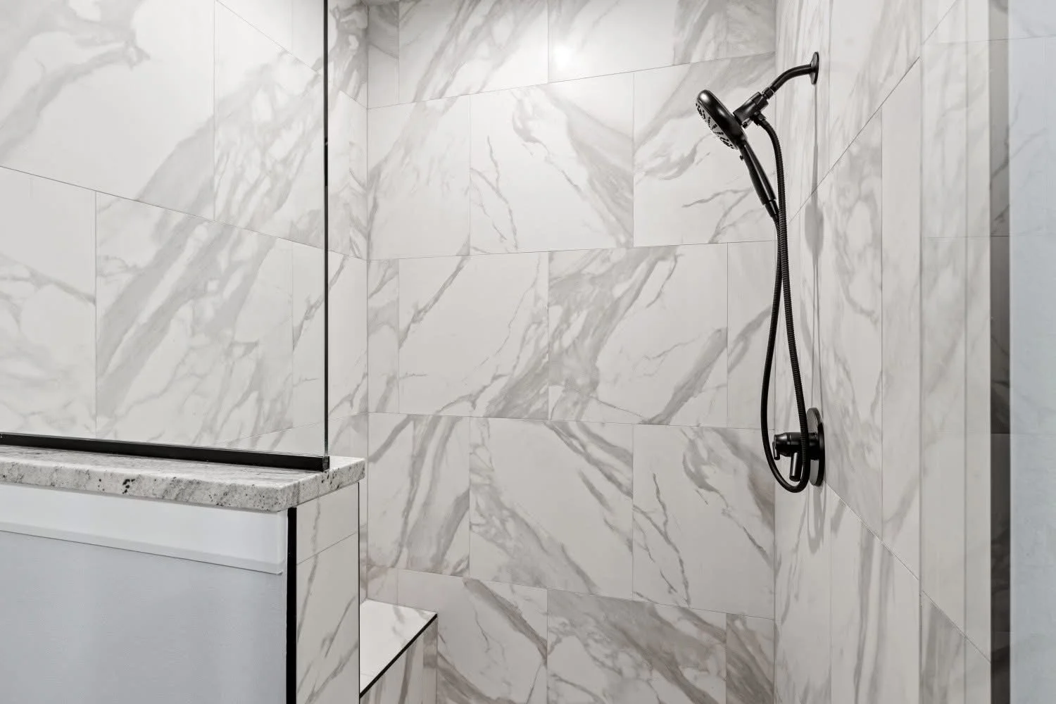 A modern shower with marble tiles on the walls and a black showerhead on the right side.