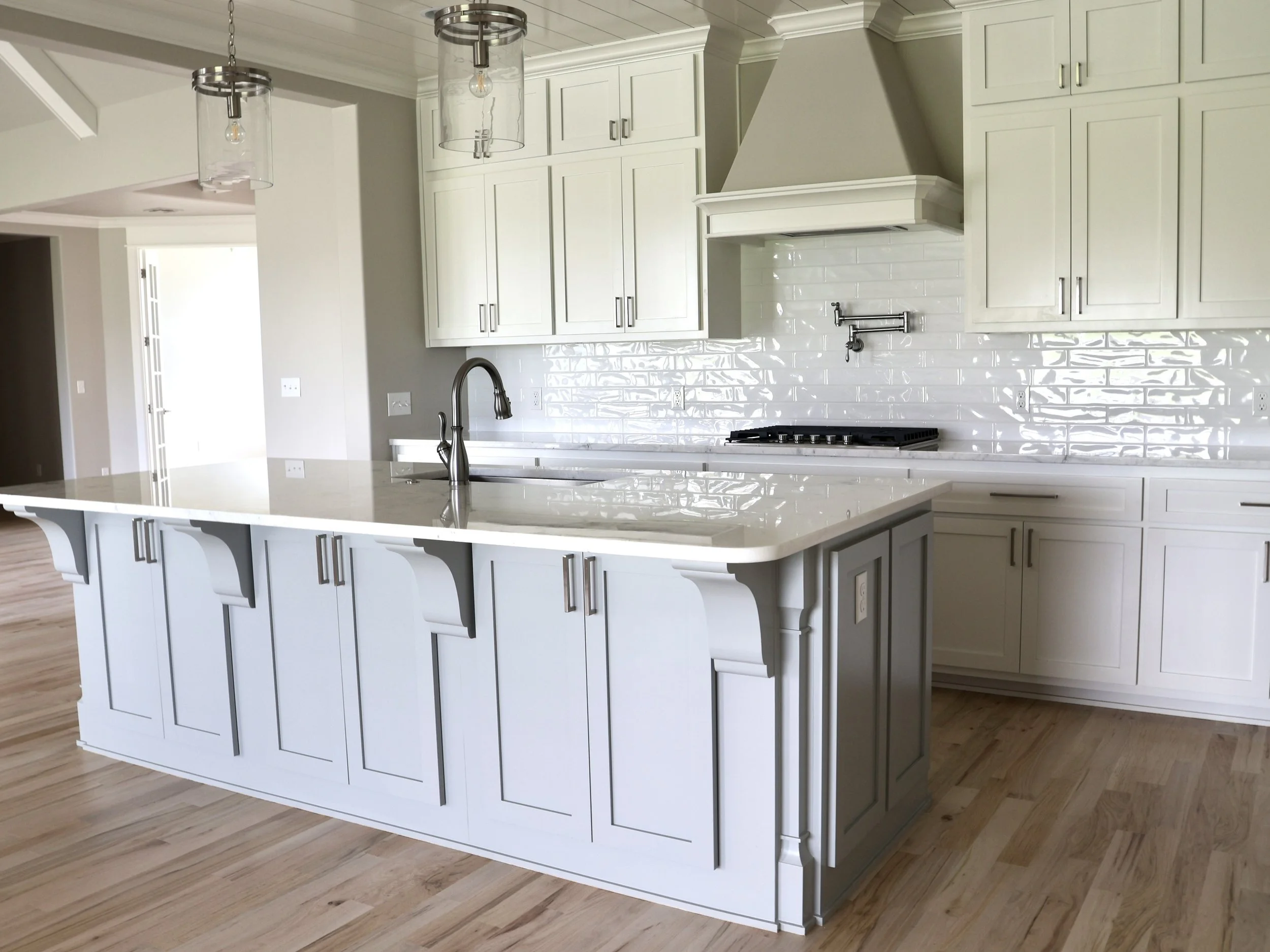 Modern white kitchen island with curved panels, marble countertop, and sink with brass faucet, surrounded by white cabinetry and wood flooring.