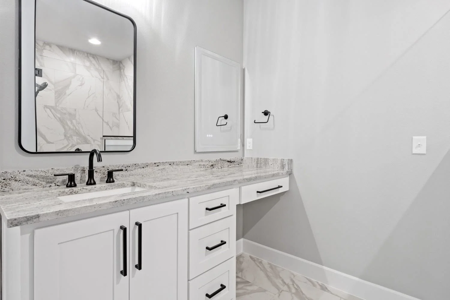 Bathroom vanity with white cabinets, a granite countertop, black hardware, a black faucet, a mirror, and a wall-mounted electrical panel.