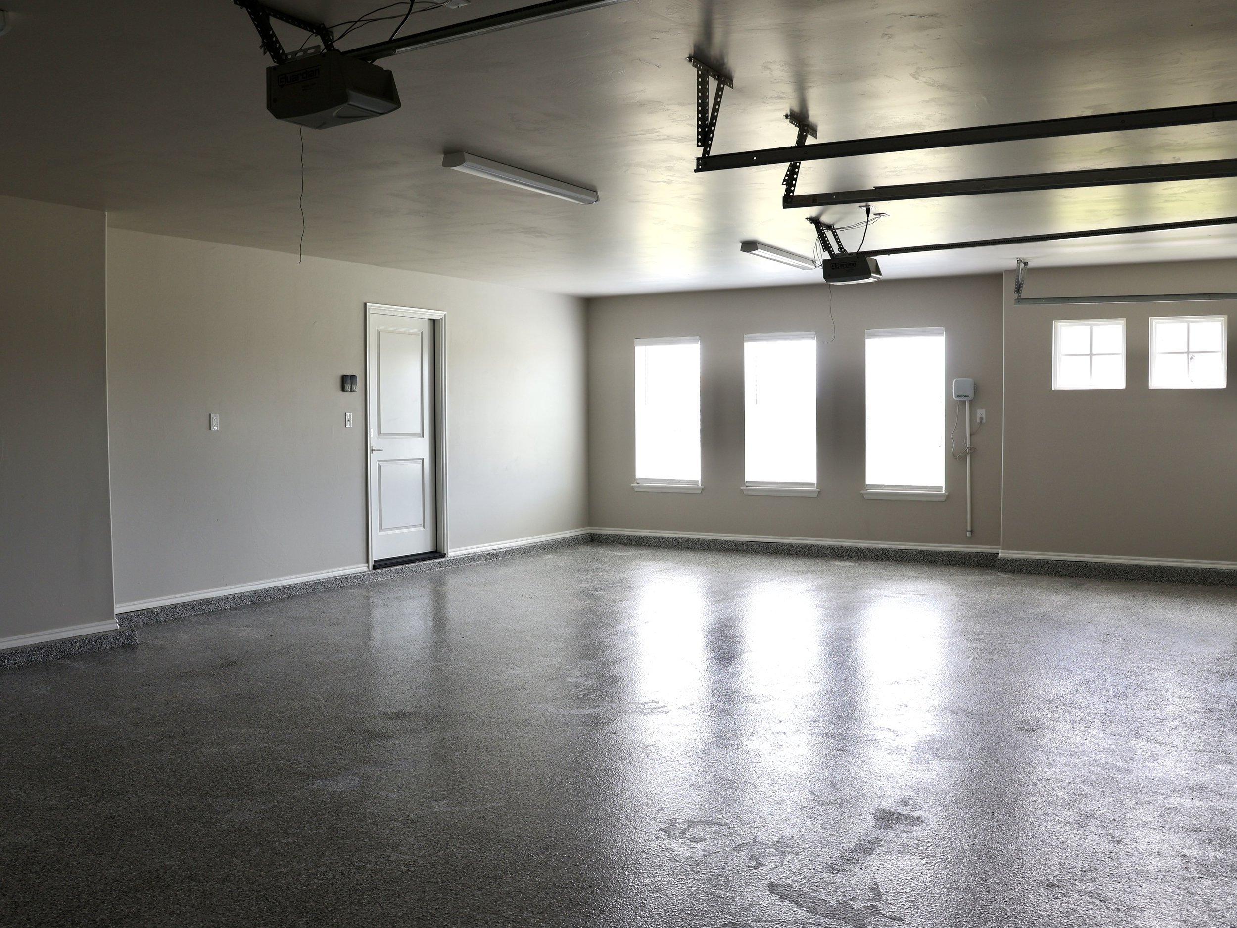 Empty garage with white walls, three windows, and garage door openers mounted on the ceiling.