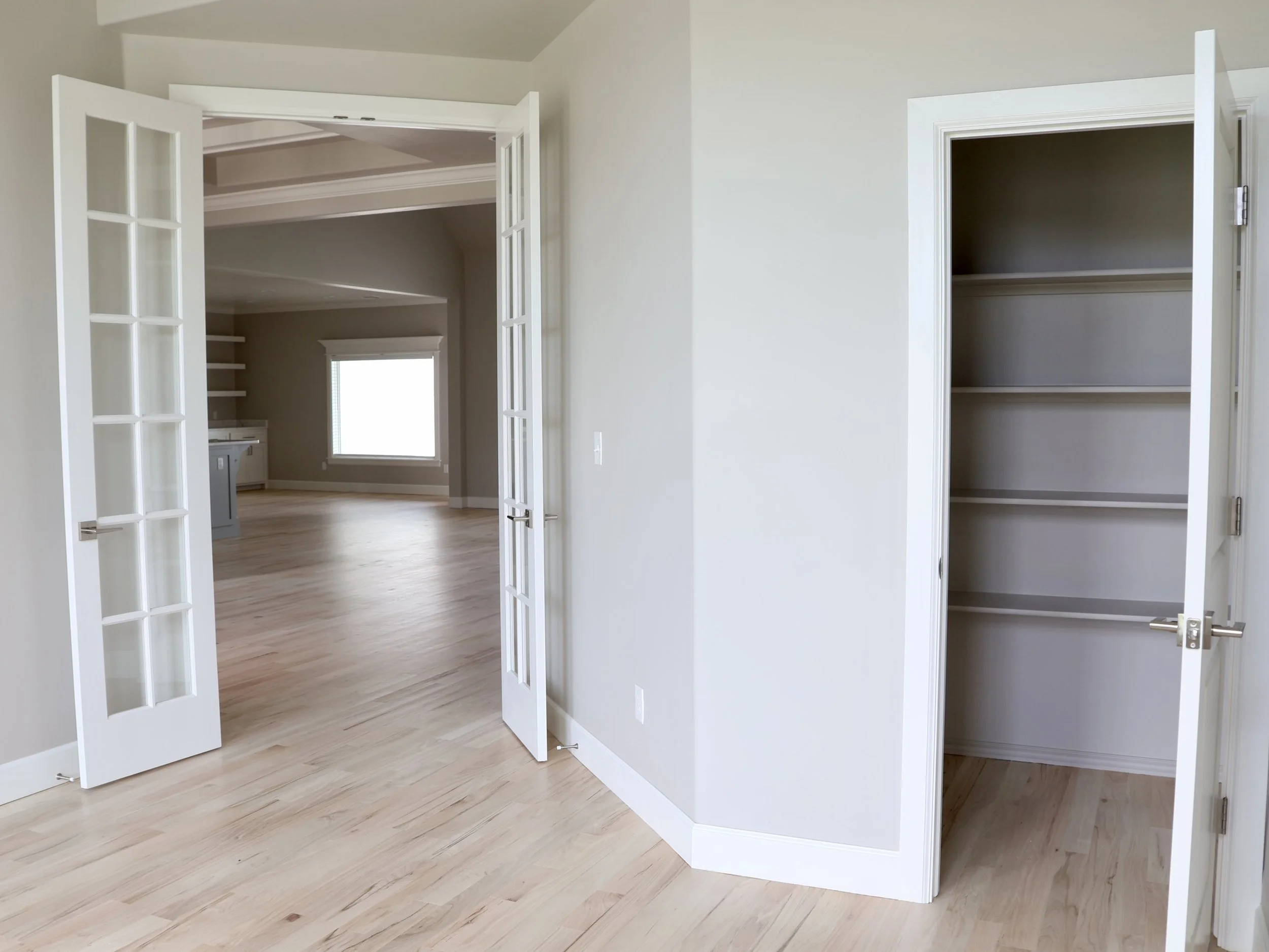 Empty room with hardwood floors, glass-paneled double doors, and two built-in closets with shelves, one on each side of the room.