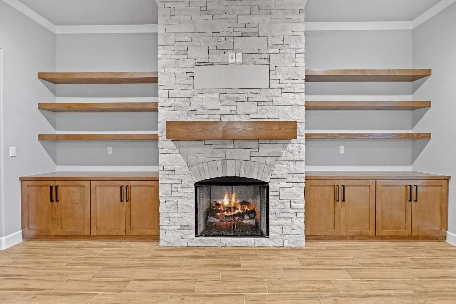 Living room with a central stone fireplace, wooden mantel, and open shelves on each side, with wooden cabinets beneath the shelves.