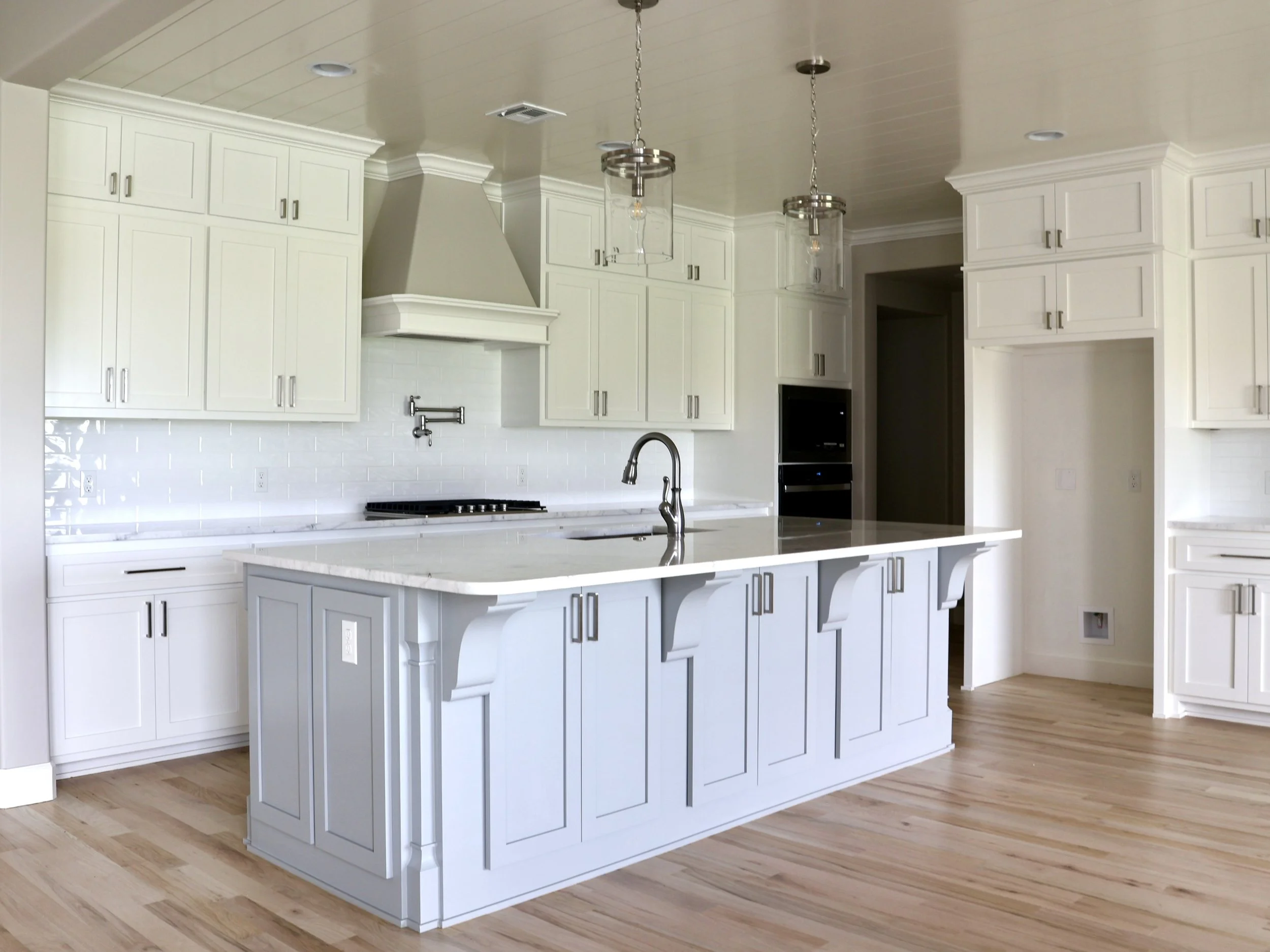 White kitchen with cabinets, a large island with a marble countertop, pendant lights, a stove, a sink, and hardwood floors.