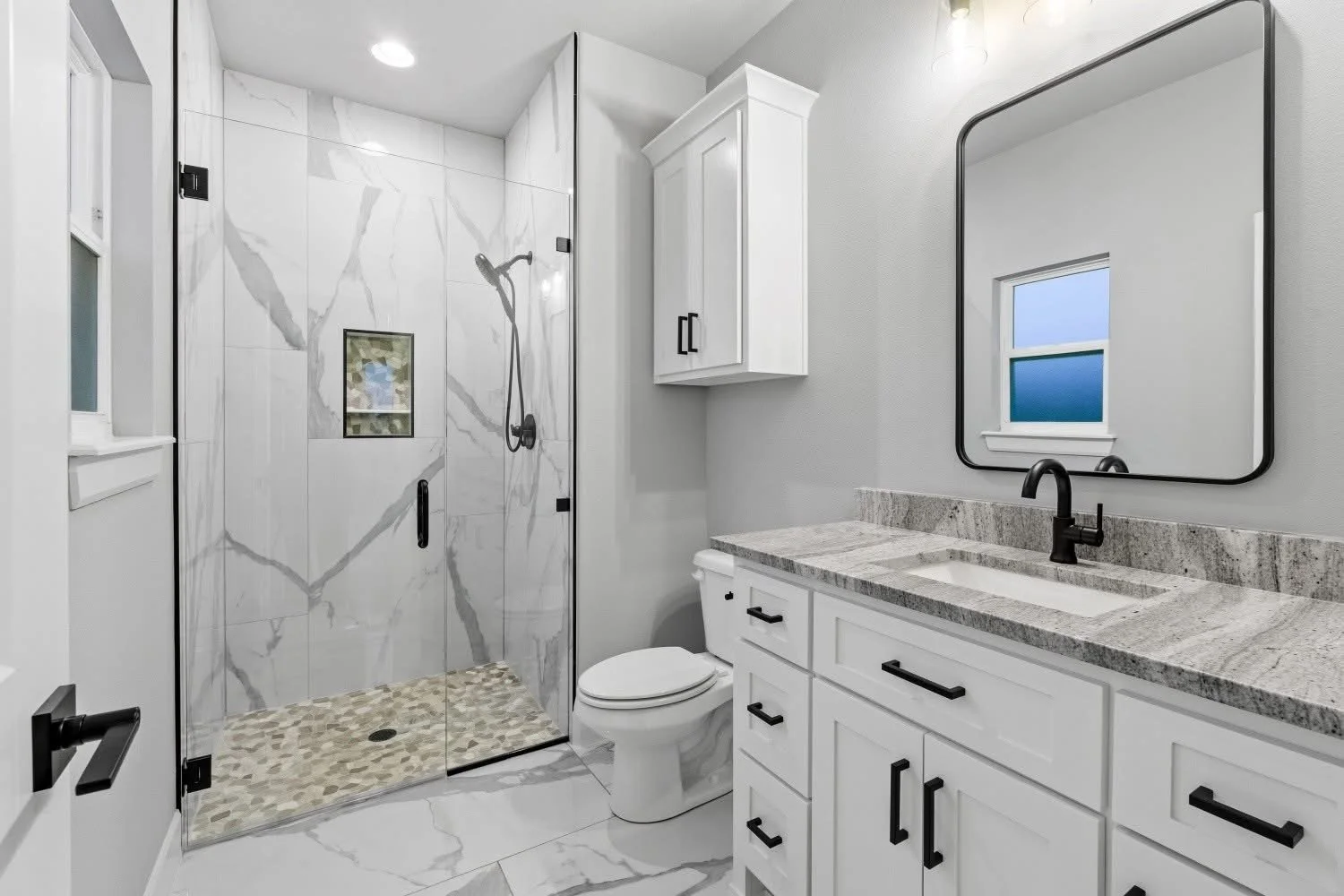 Modern bathroom with a glass shower enclosure, white vanity with marble countertop, black hardware, a mirror, and a small window.