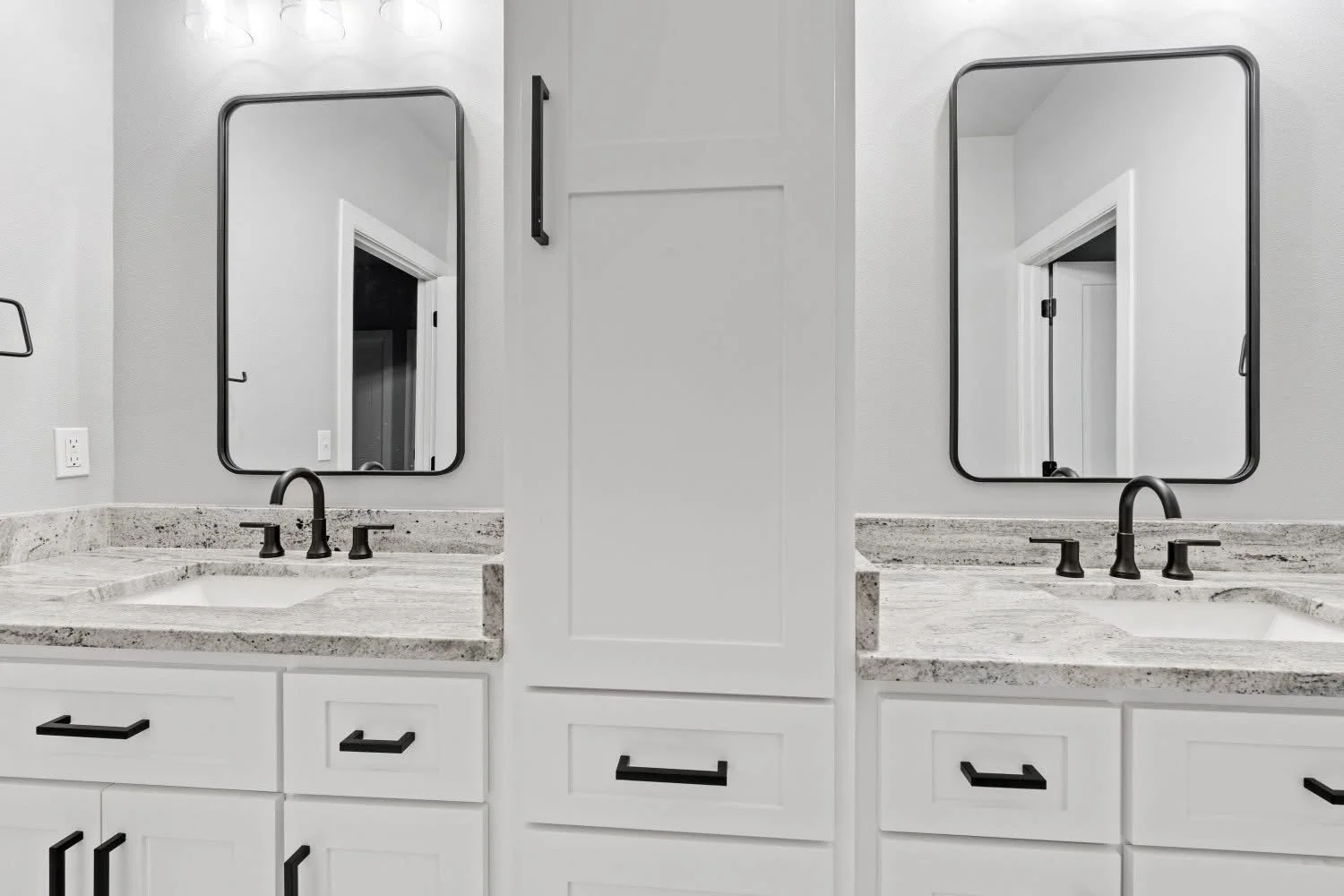 Close-up of a modern bathroom double vanity with two rectangular mirrors, black faucets, and white cabinetry with black handles.