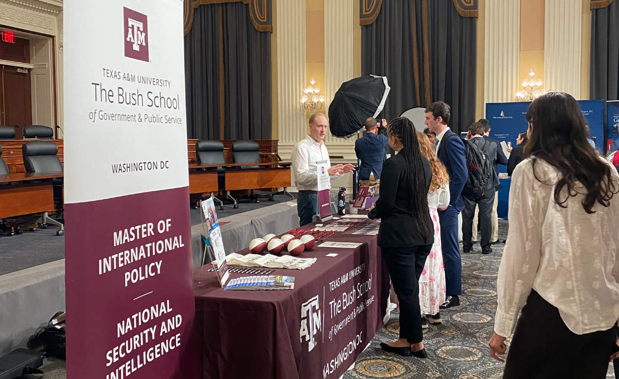 People attending an information session or career fair at Texas A&M University's Bush School of Government & Public Service in Washington, D.C. The booth displays materials related to the Master of International Policy program.