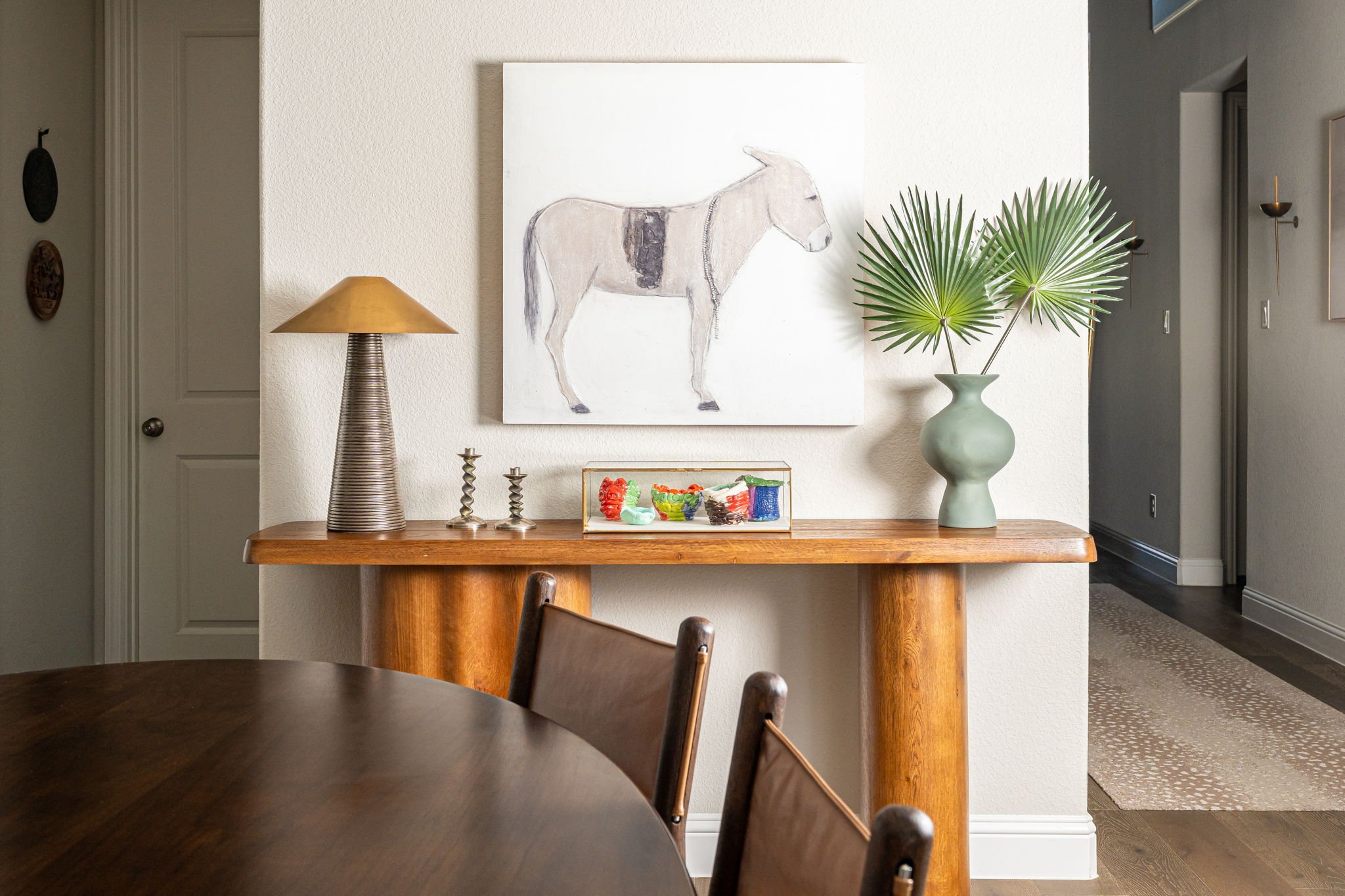 Dining room styled with wood credenza topped with metal lamp colorful vases and palm branches. 