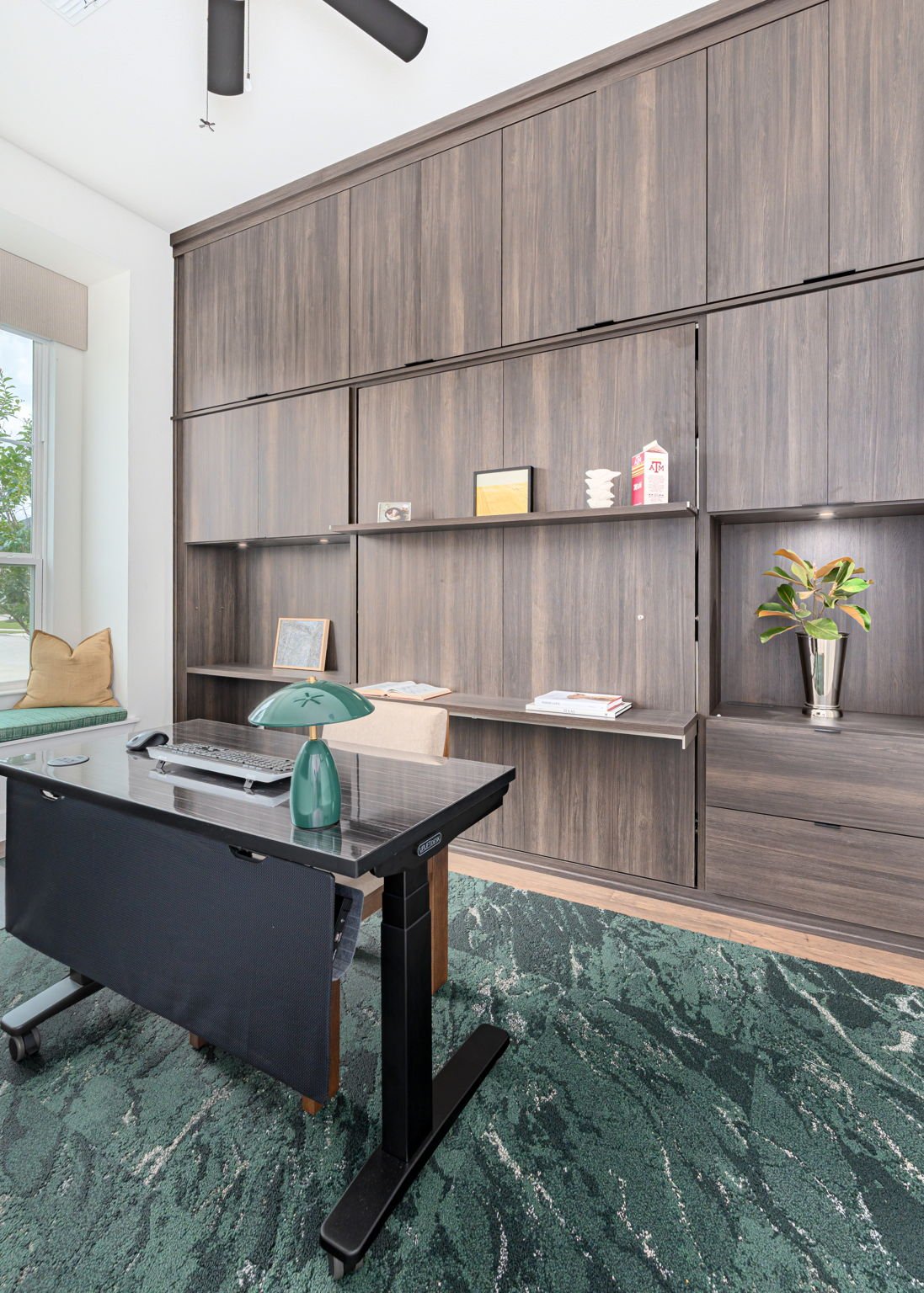 Home office with dark wood built-ins on one wall and dark green rug