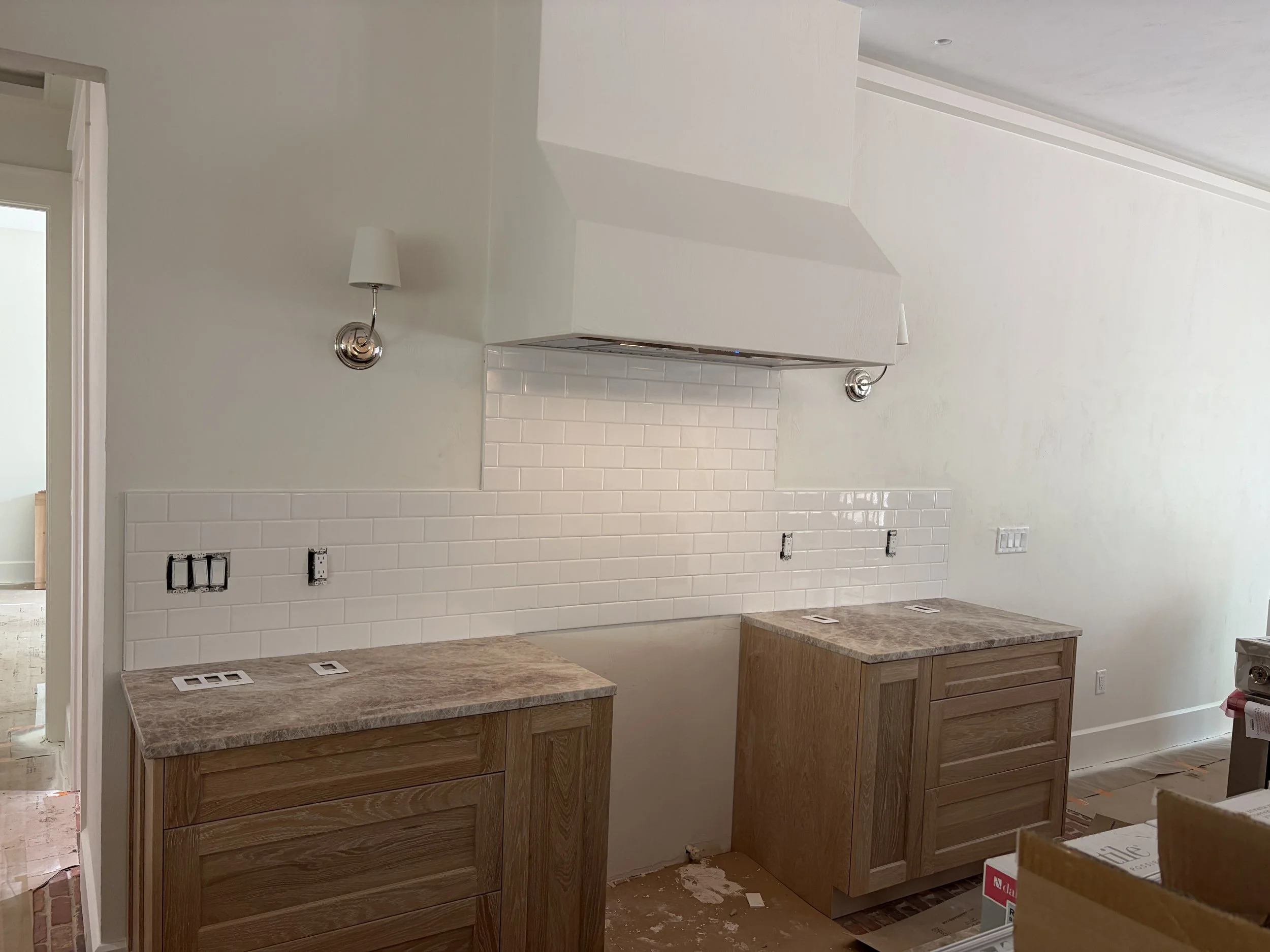 Kitchen in a new construction home in a semi finished stage with white plaster walls subway tile backsplash, brown and beige natural stone countertops and light wood cabinets.
