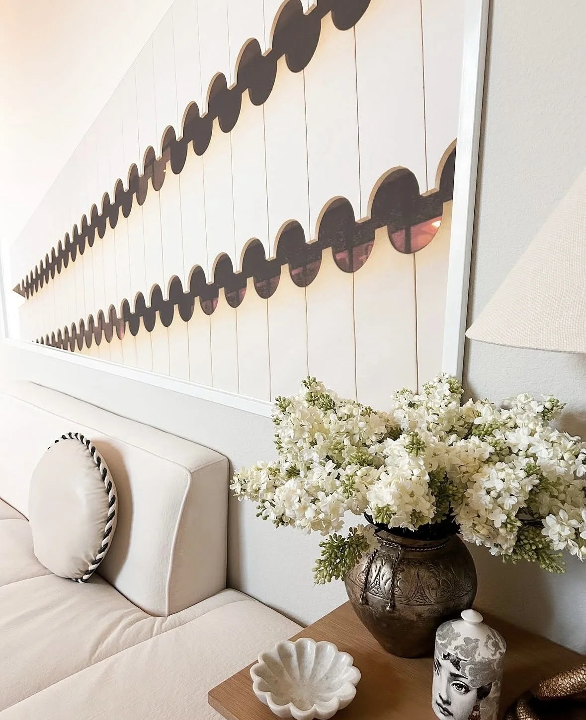 Home office in Frisco, Texas, decorated by interior designer Brooke Bundy Designs. Photo shows oversize art on the wall, a cream colored couch with a round pillow, faux flowers, a flower-shaped marble bowl and a side table.