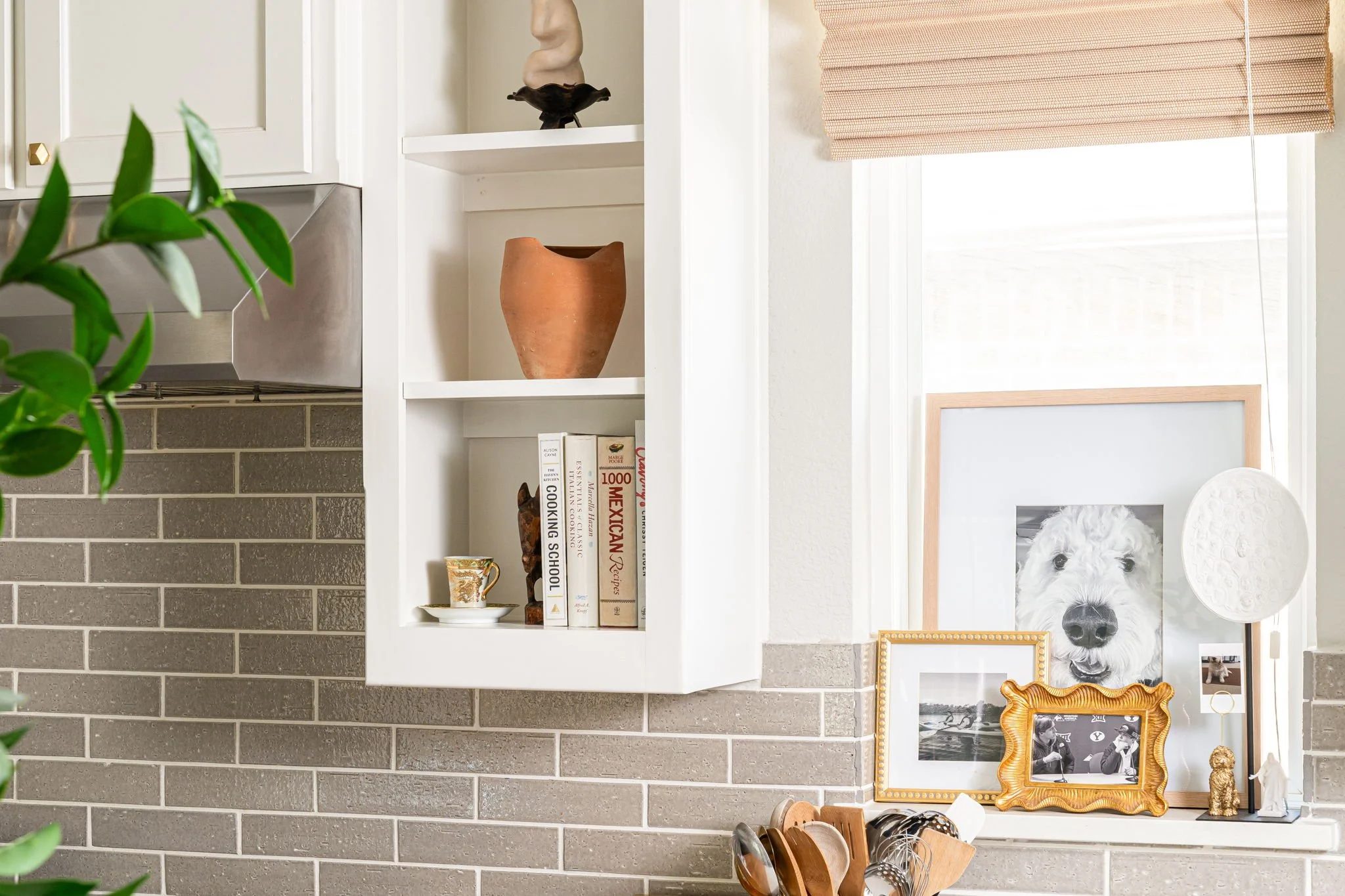 kitchen shelves styled with cookbooks and pottery. framed black and white photos are on the windowsill
