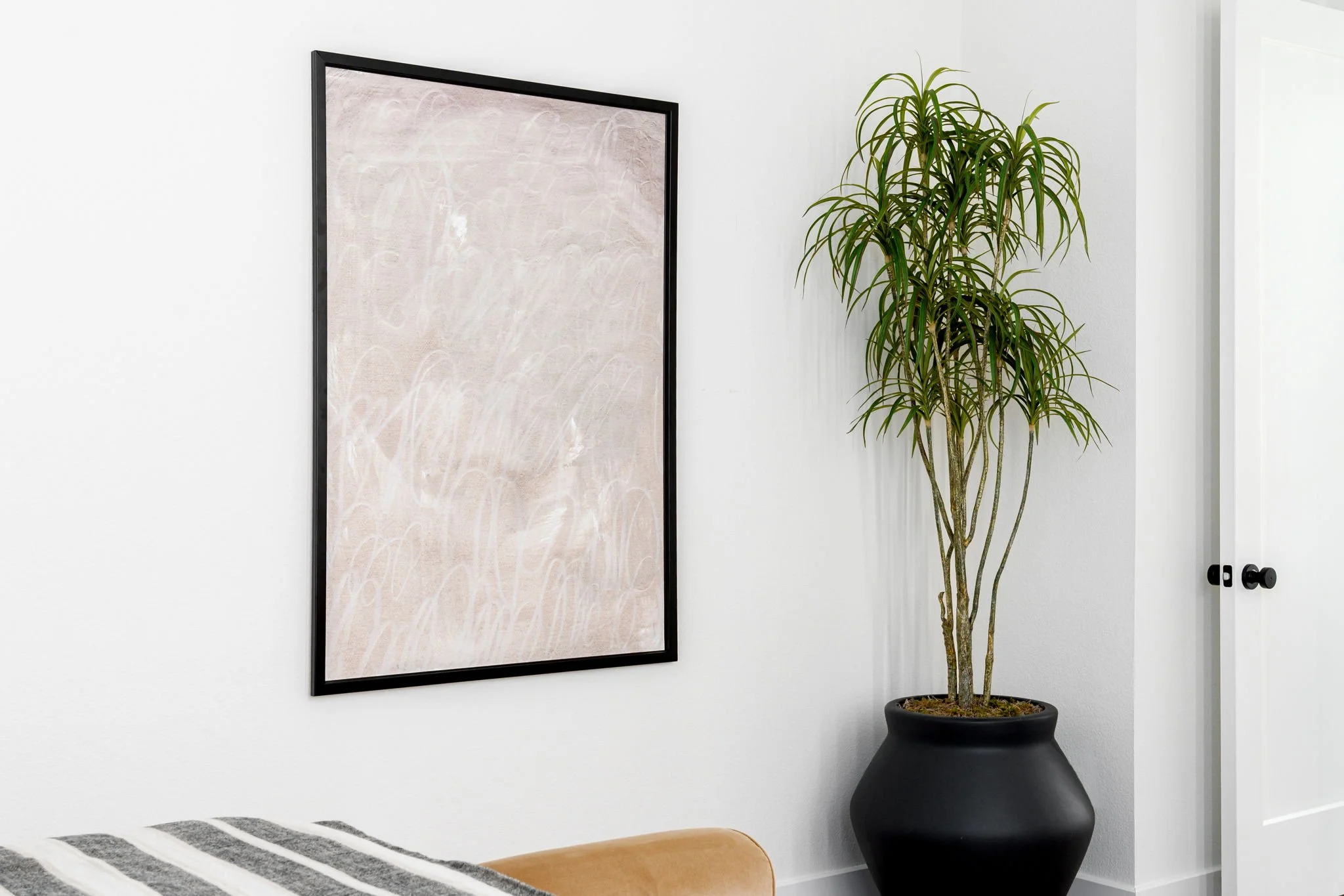 corner of primary bedroom with white walls, large abstract artwork with a black frame and a tree in a black pot