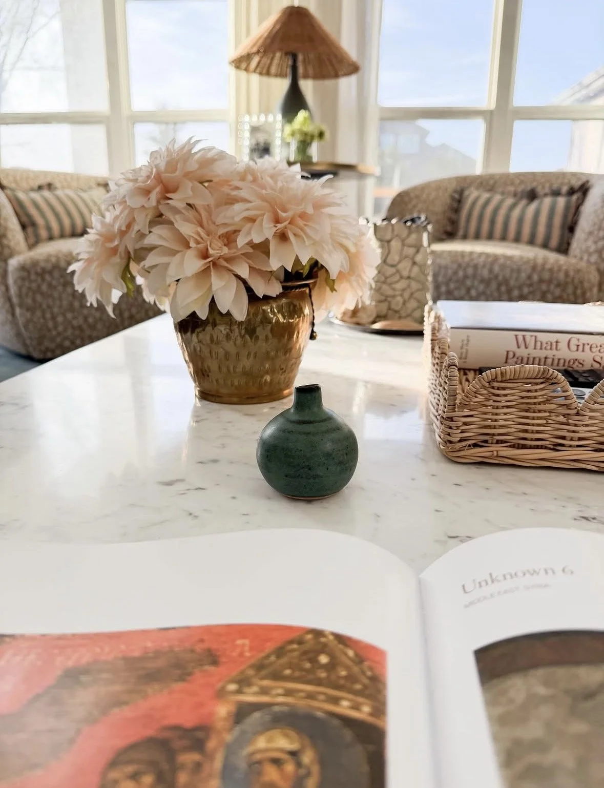 A living room in Frisco, Texas, decorated by interior designer Brooke Bundy Designs. Photo shows chairs with custom fabric, throw pillows, pink flowers in a gold jar, a woven tray, a green jar, and a marble coffee table.