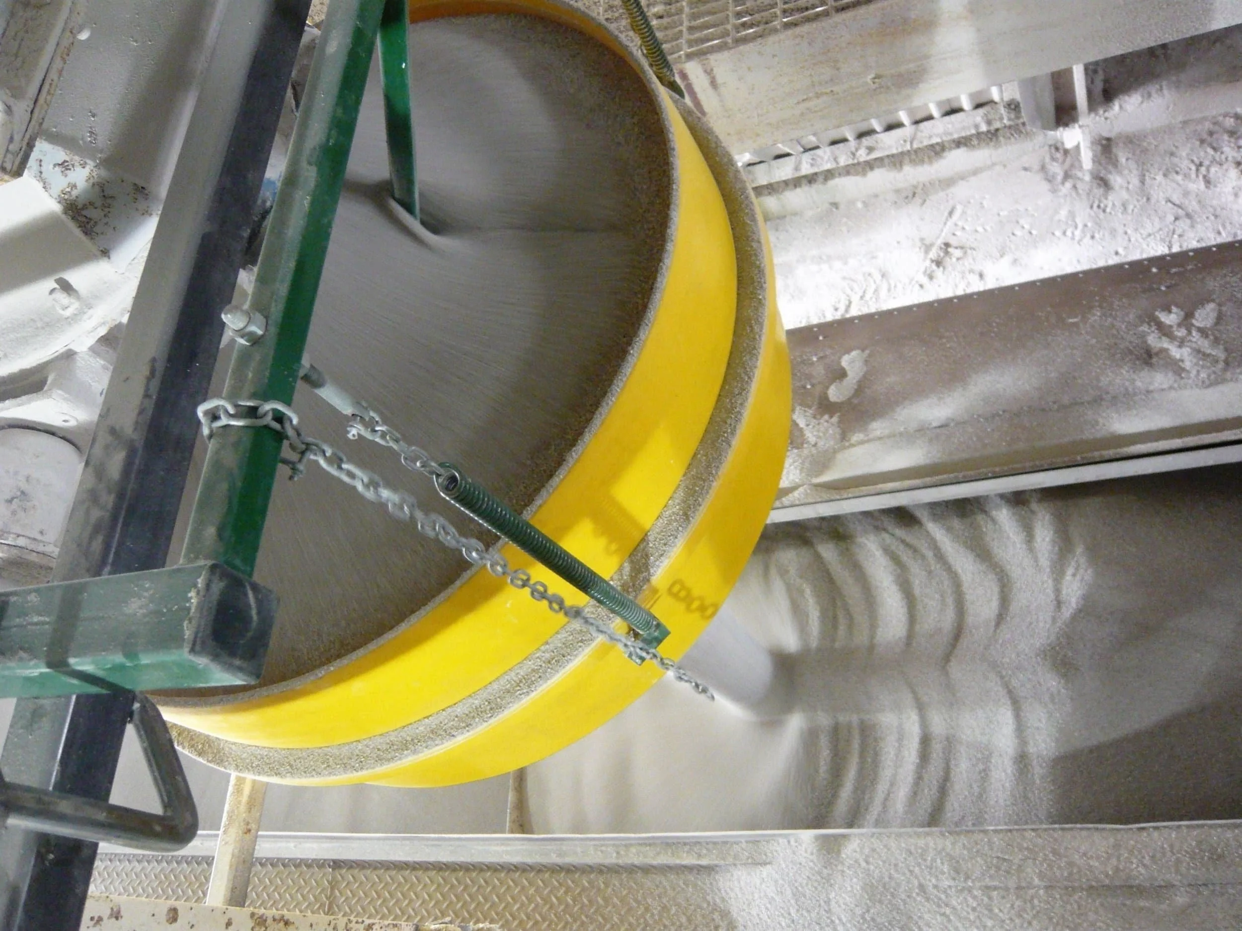 A construction site with a dust suppression hopper pouring white granular material into a loading area.