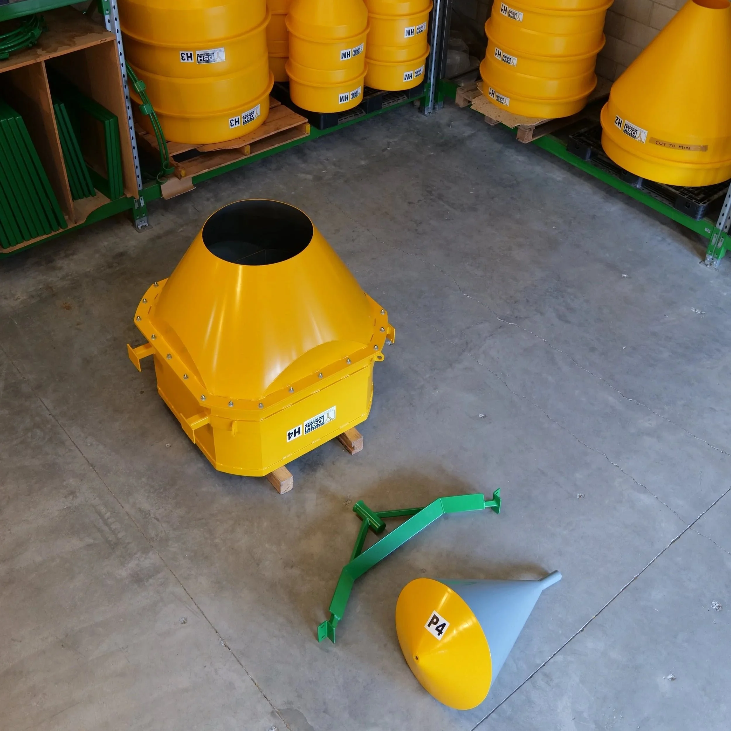 Large yellow industrial dust suppression hopper with green metal support and plug on a concrete floor in a workshop.