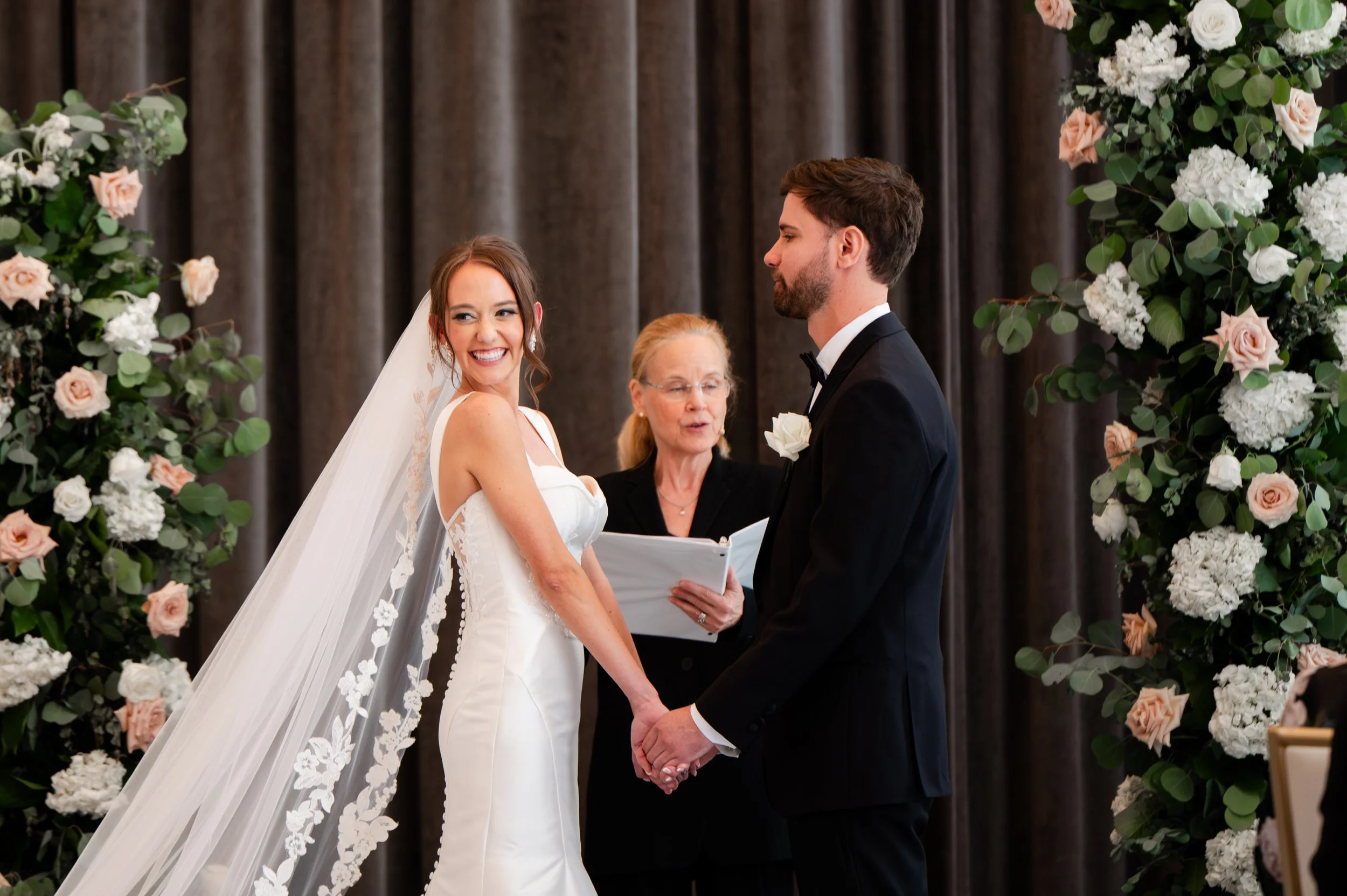 Image of smiling bride and groom at Hotel Monaco, surrounded by floral pillars filled with greenery and roses.