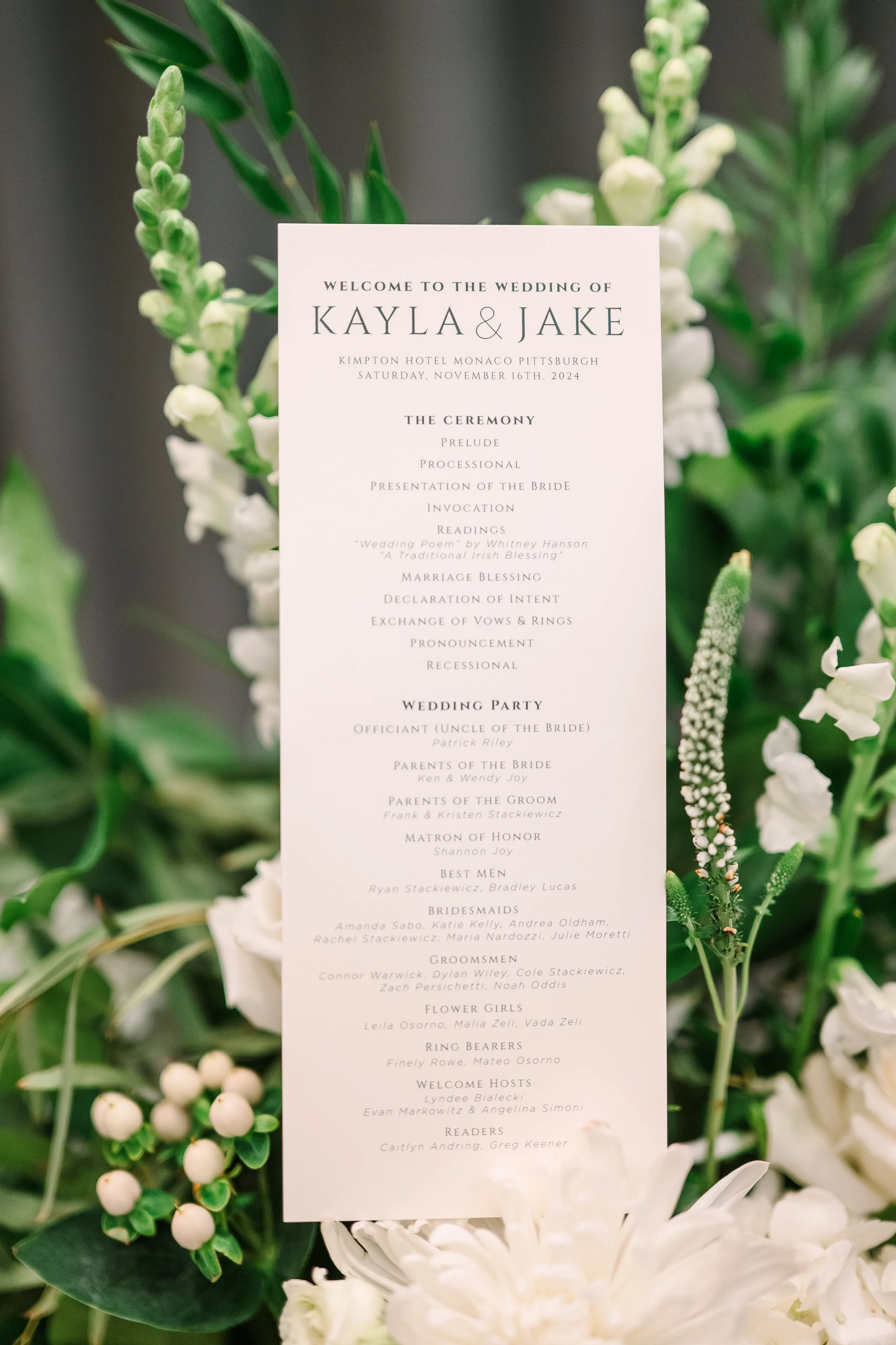 Detail image of the wedding itinerary, surrounded by greenery and white flowers in Hotel Monaco.