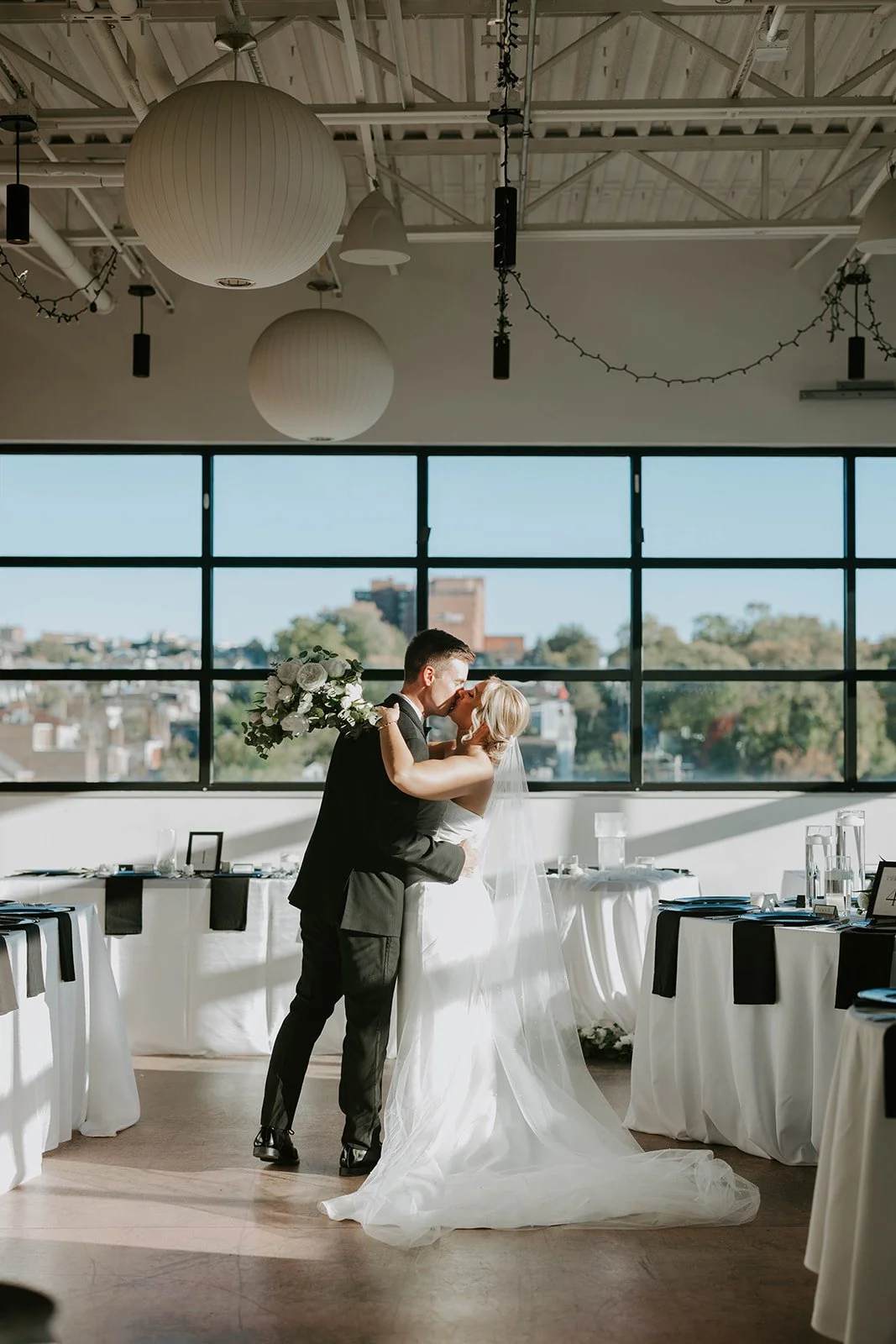 Happy couple, kissing in the unique Lawrenceville venue, Over Eden, with the city of Pittsburgh in the background.