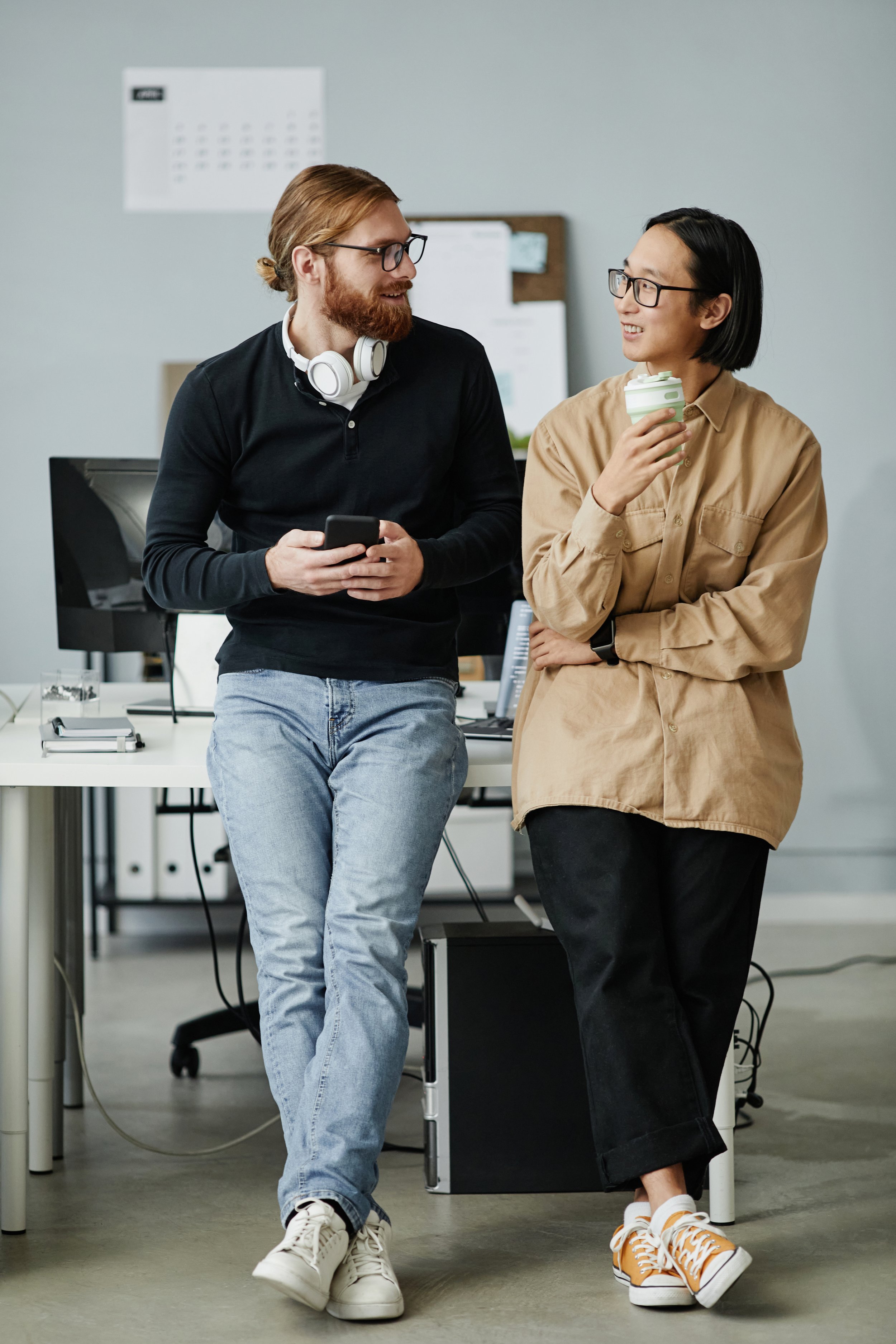 A woman with glasses and a yellow beanie smiling behind the coffee machine at a cafe, holding a portafilter.
