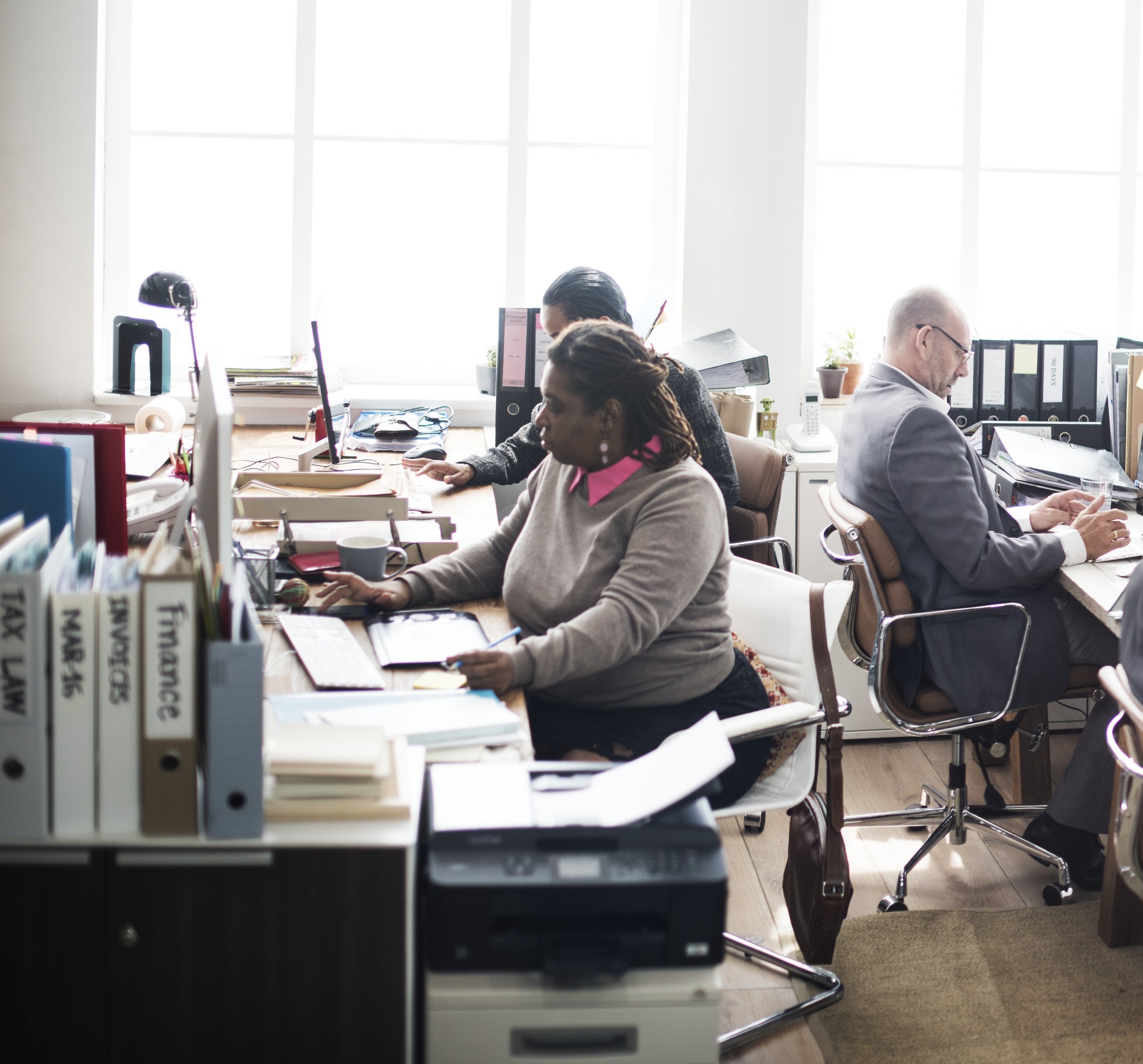 A woman smiling at her laptop in a bright, white room with a white cabinet and decorative items in the background.