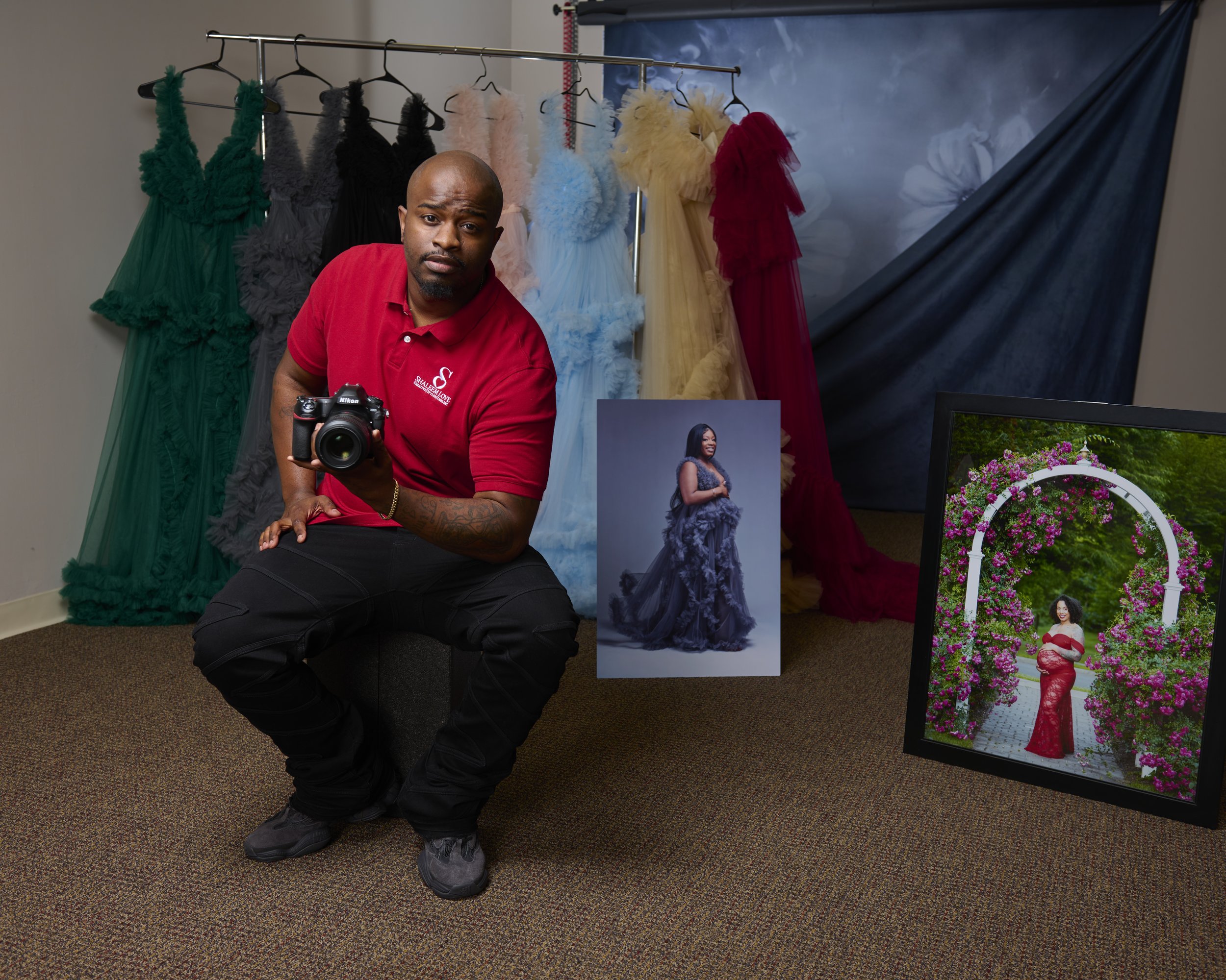 Photographer Shaleem Love in studio with maternity gowns and framed client portrait