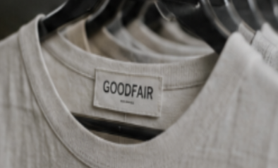Close-up of a beige t-shirt with a 'GOODFAIR' label, hanging among similar shirts.