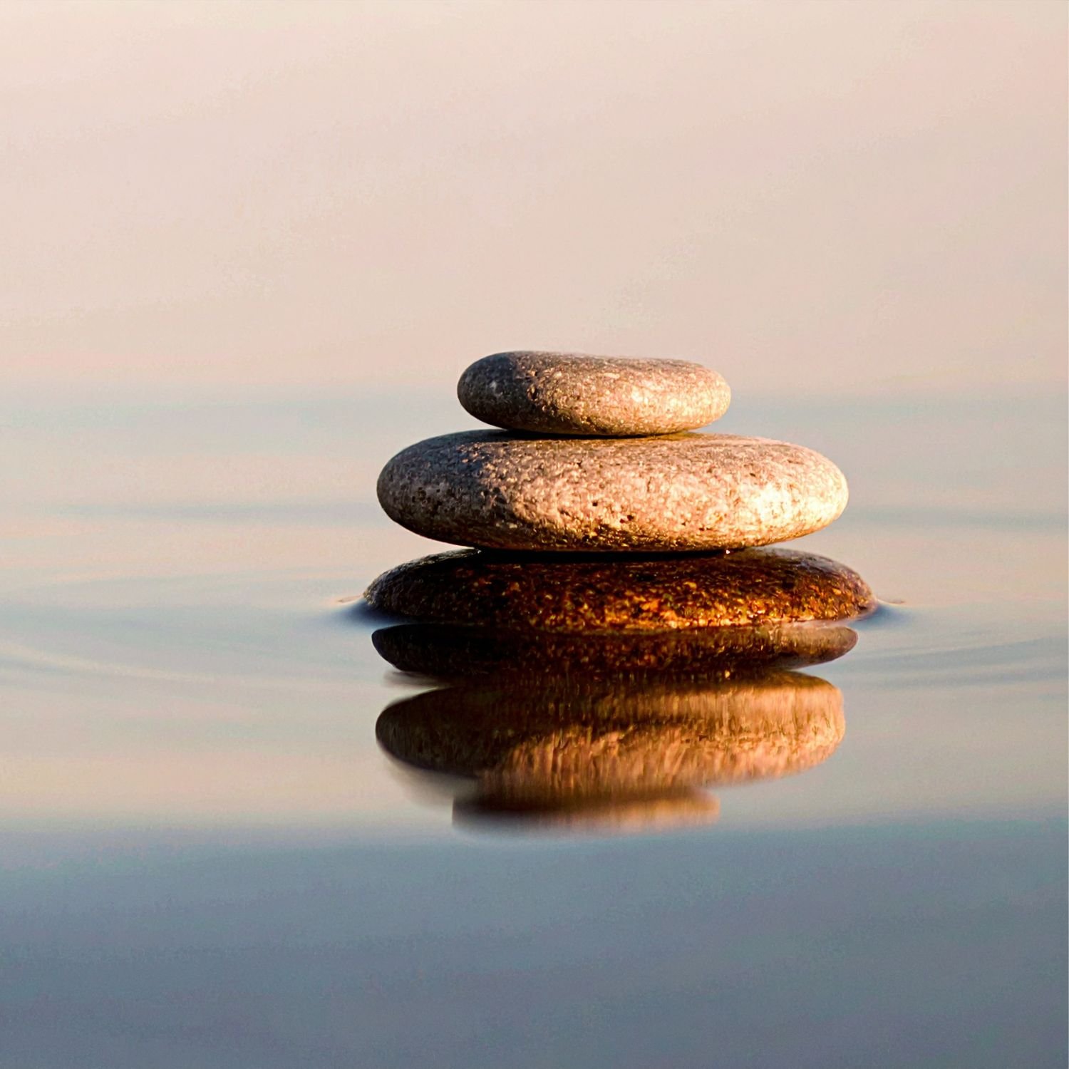 Four stacked stones reflected in calm water at sunset or sunrise.