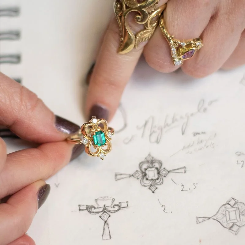 Melissa showcasing an emerald ring and the drawings that inspired it.