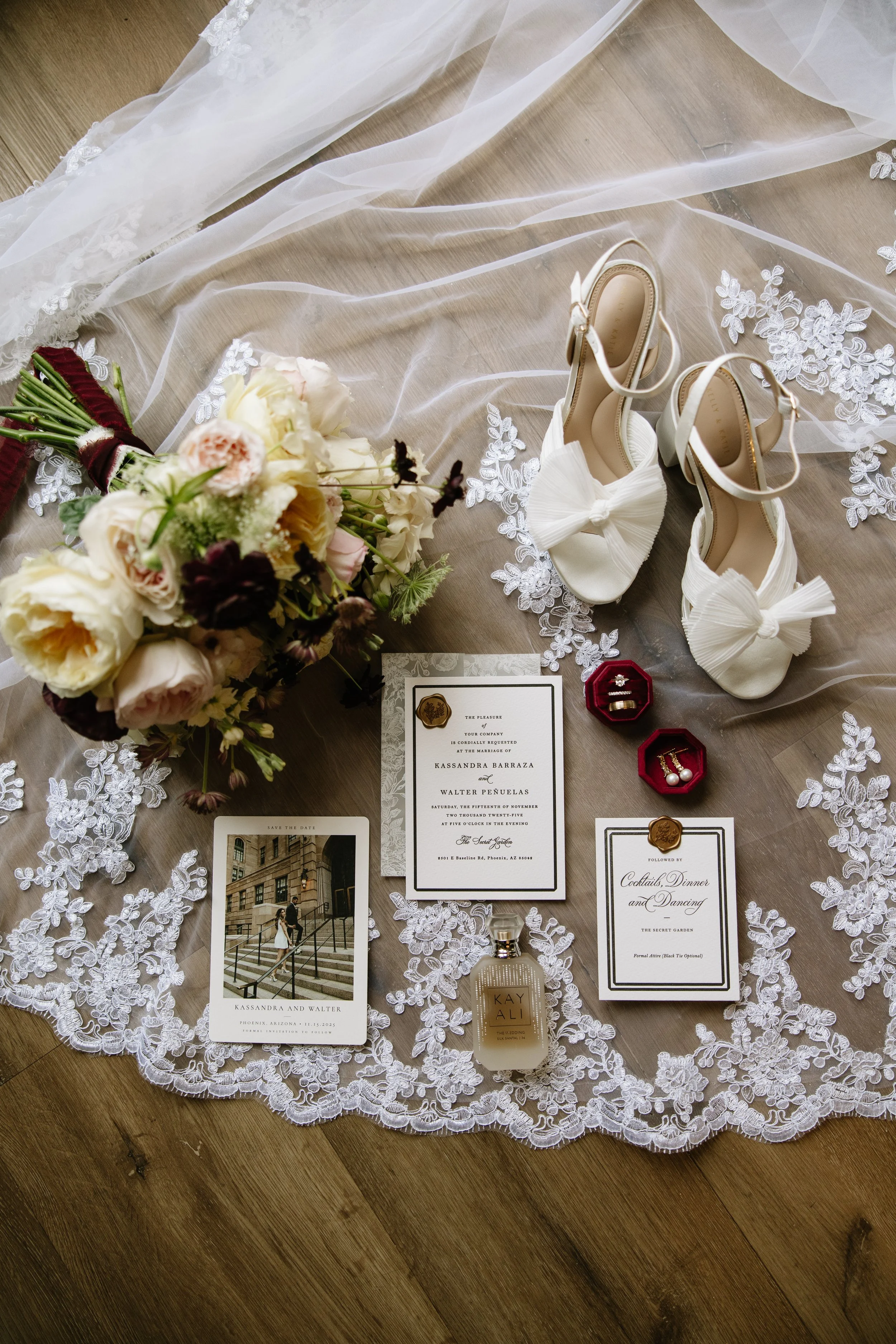Wedding invitation, bridal shoes, bouquet, perfume, jewelry, and event details on a lace tablecloth.