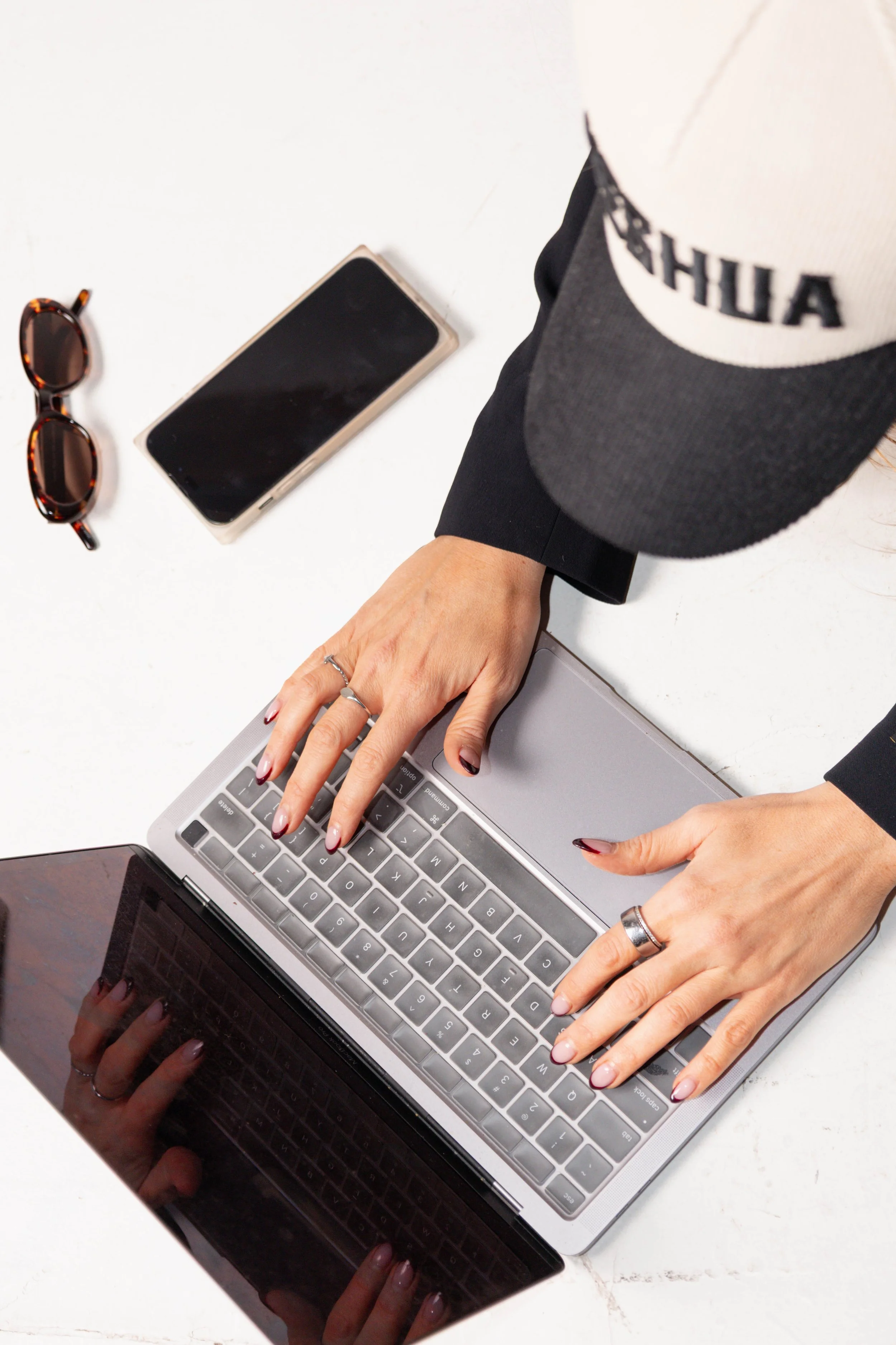 Woman with curly hair and glasses laughing and holding her chest, wearing a light gray hoodie.