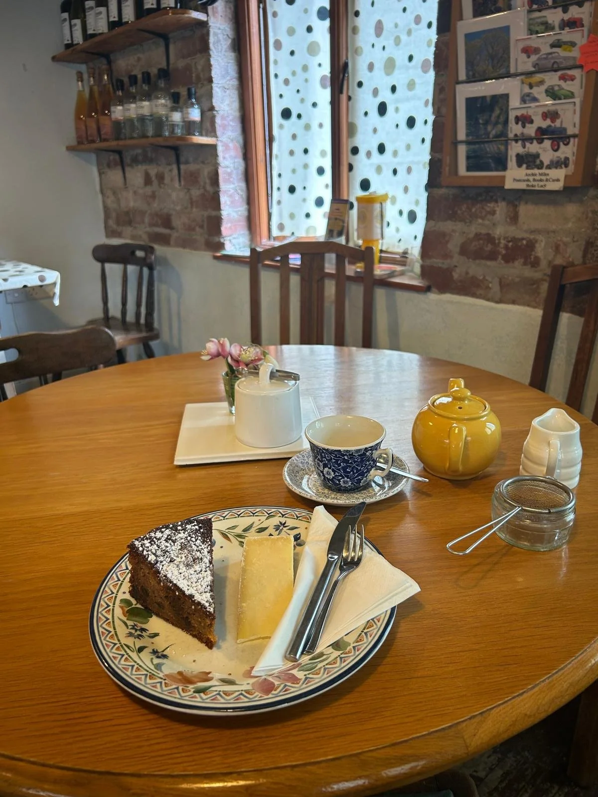 Herefordshire Apple Cake and Cheese on a plate, with a pot of tea, teacup and saucer placed behind. All on a wooden table