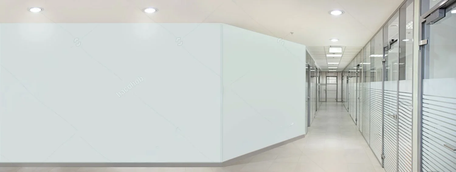 Empty office corridor with glass and metal partitions, overhead lighting, and beige tiled floor.