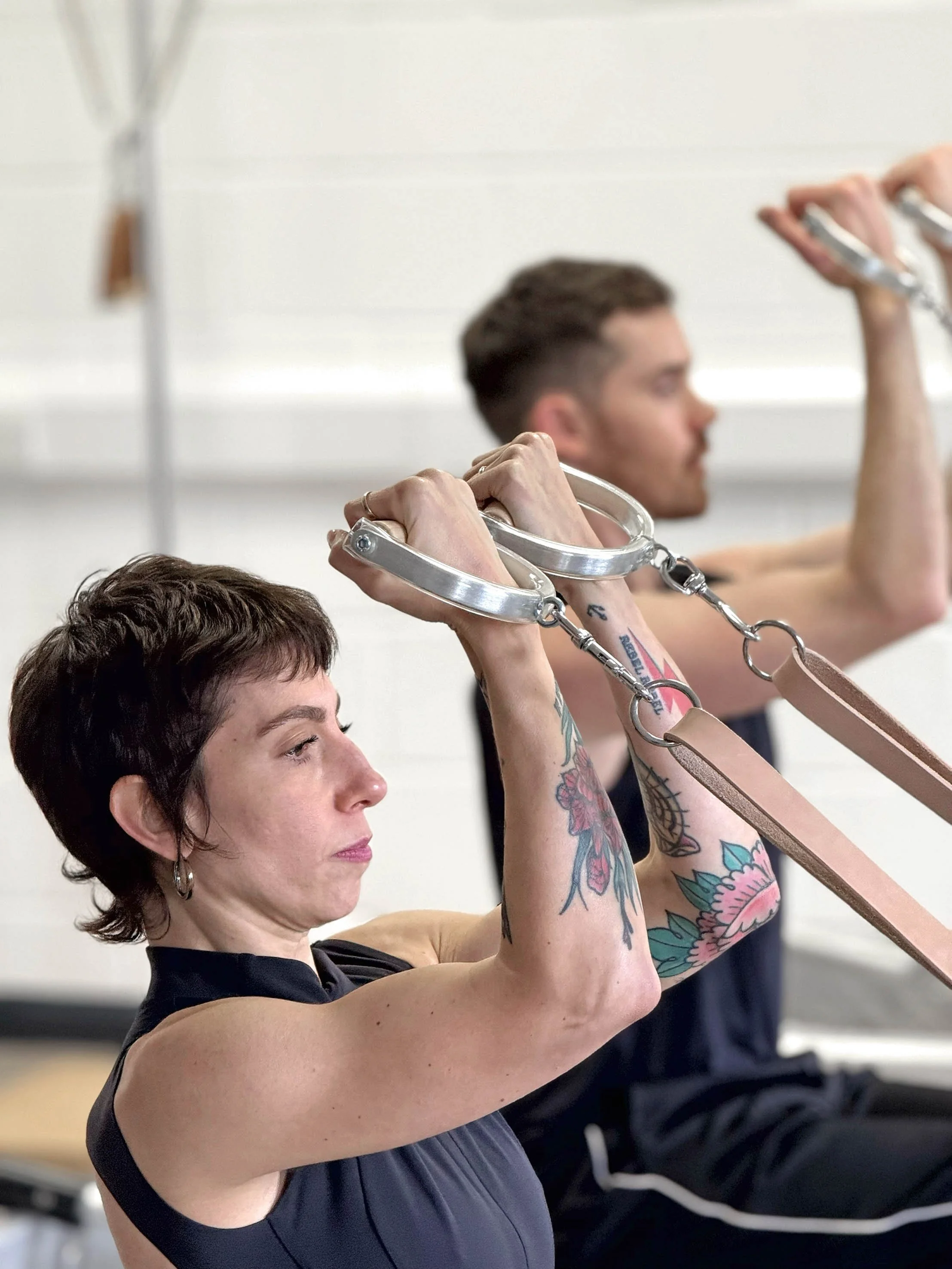 A woman and a man exercising together, both holding ethe reformer handles in front of them.