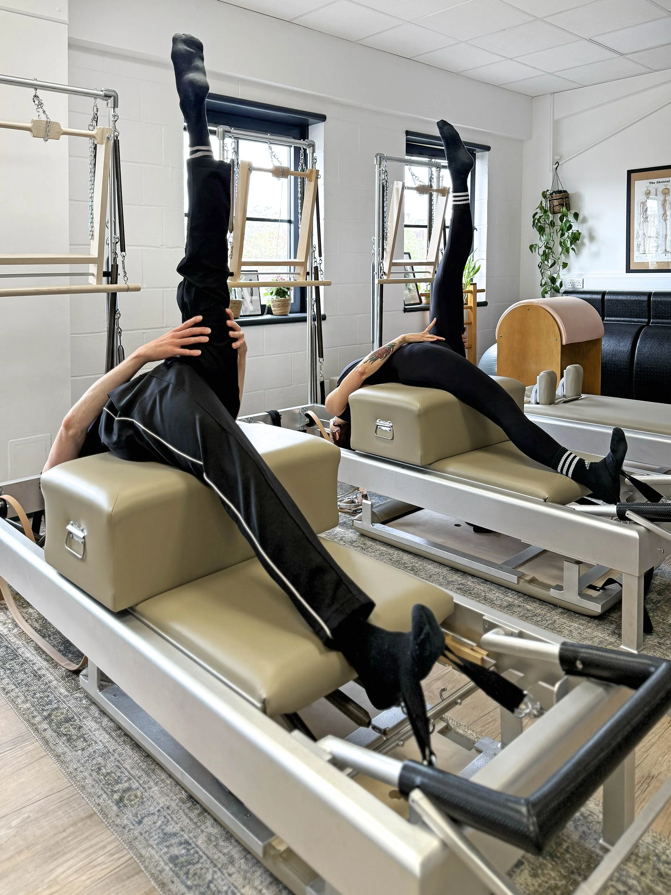 Two people performing the tree exercise on the short box on the reformer. A classical exercise true to the method.