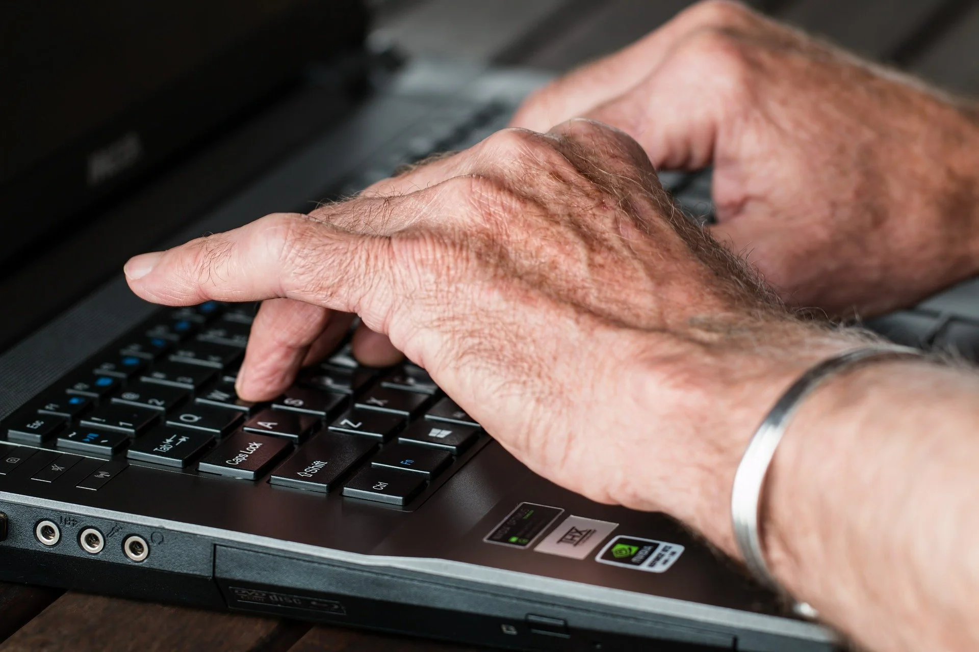 Close-up of elderly person's hands typing on a laptop keyboard.