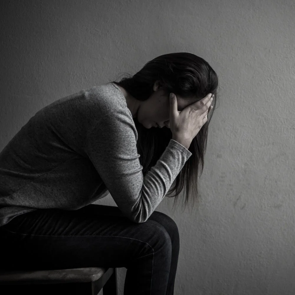 A woman sitting on a chair with her head in her hands, appearing distressed or upset.