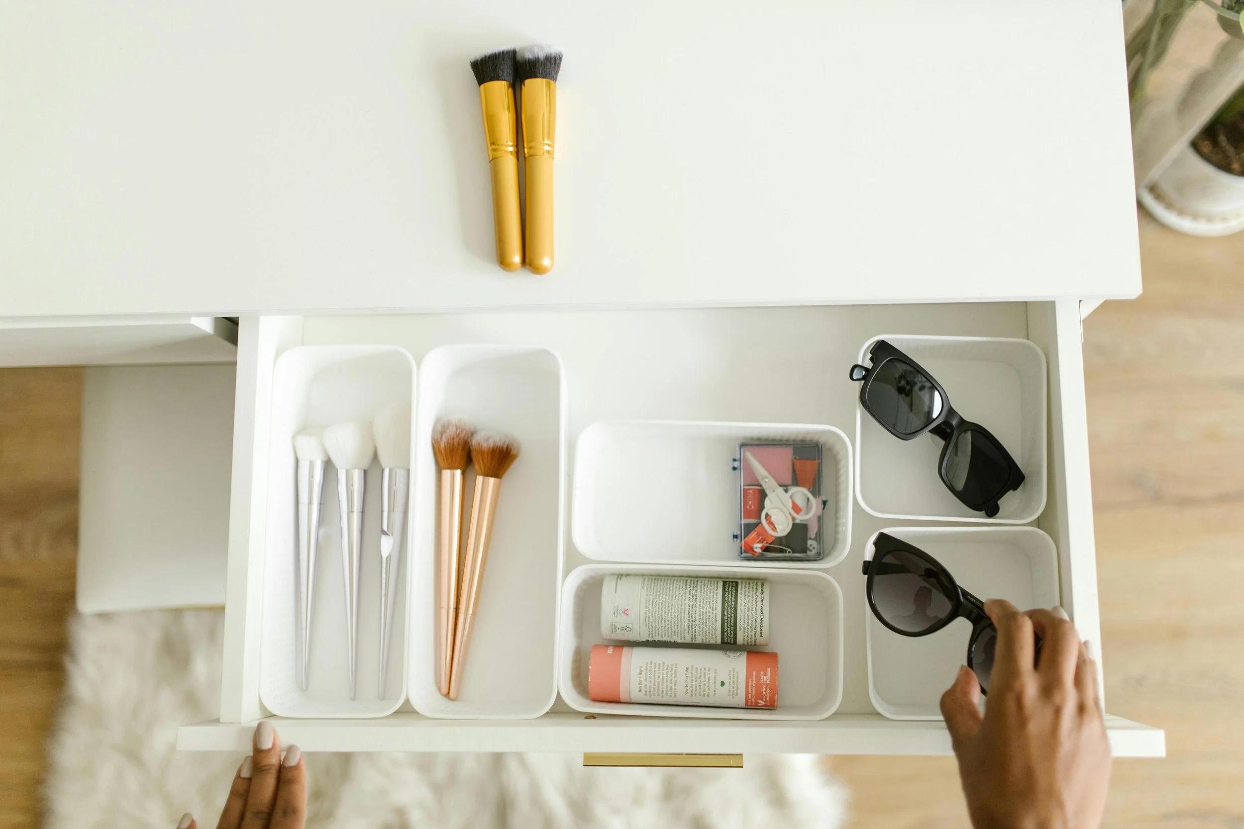 organizing a drawer with makeup brushes, sunglasses, and a sewing kit