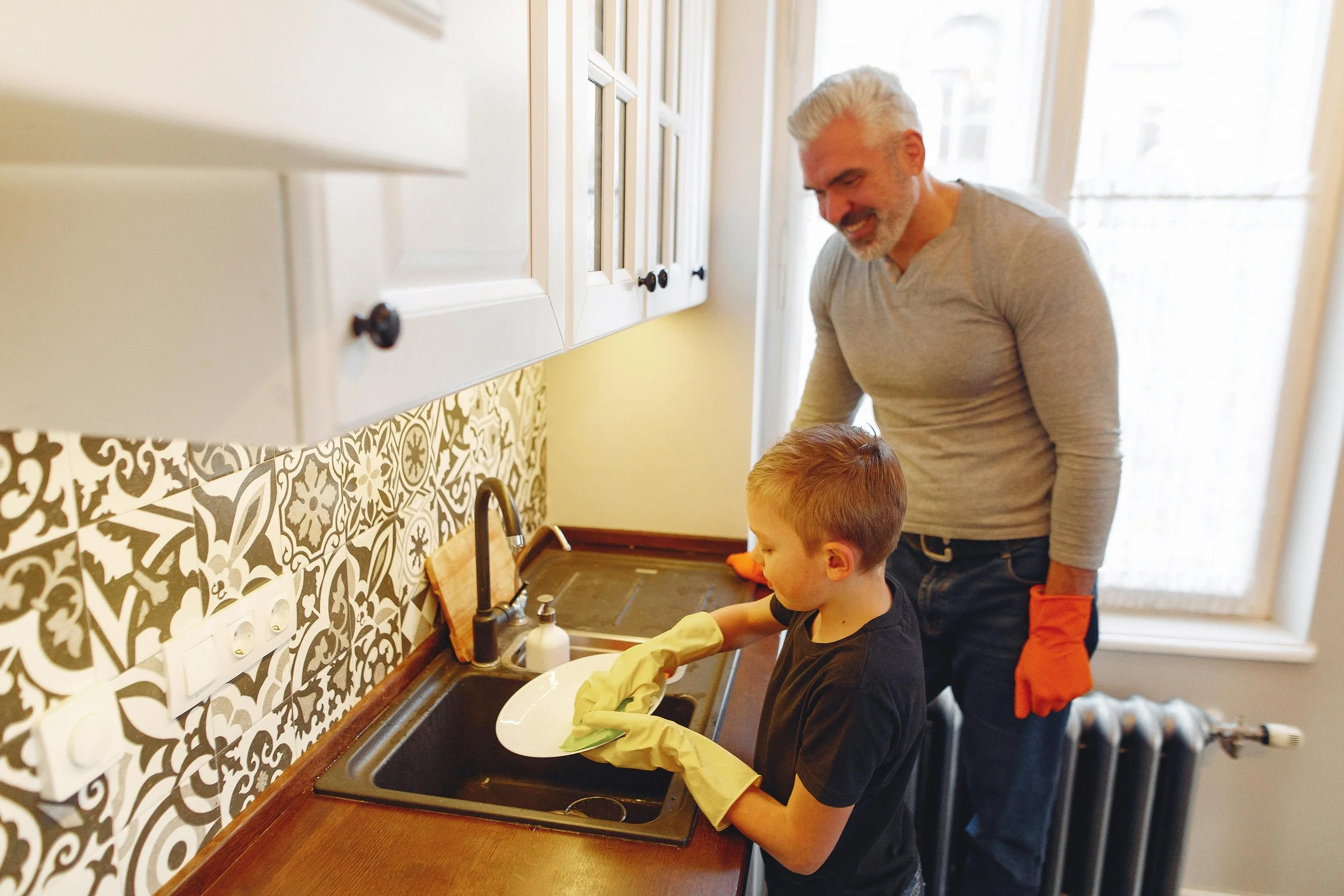 boy doing dishes supervised by father