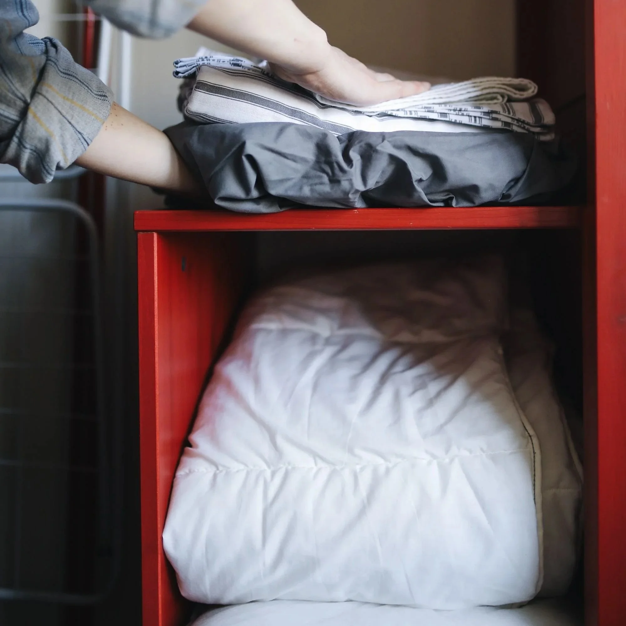 hands placing bedding on a shelf above a folded white comforter