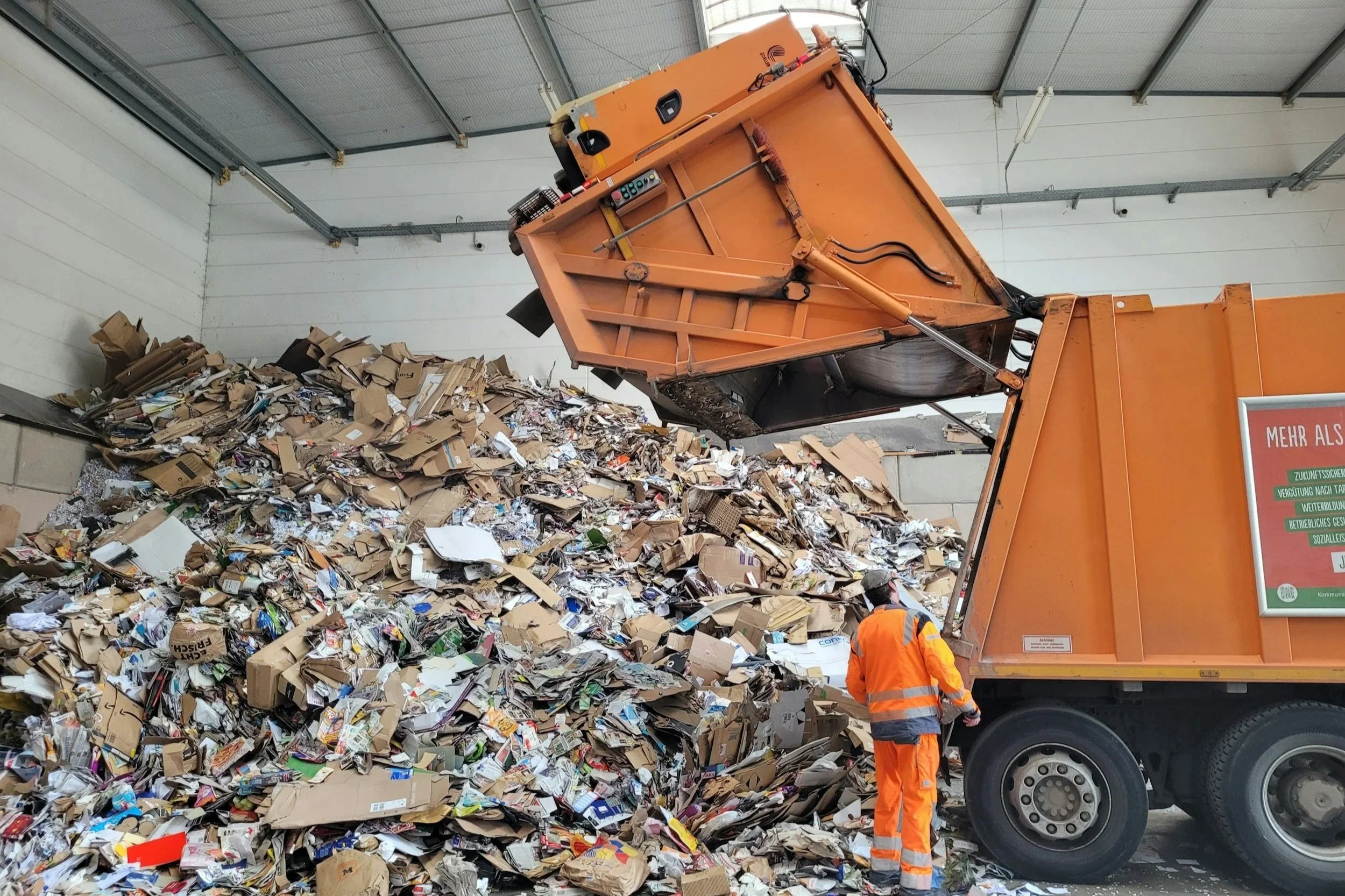 A garbage truck dumping trash in a pile in a warehouse.