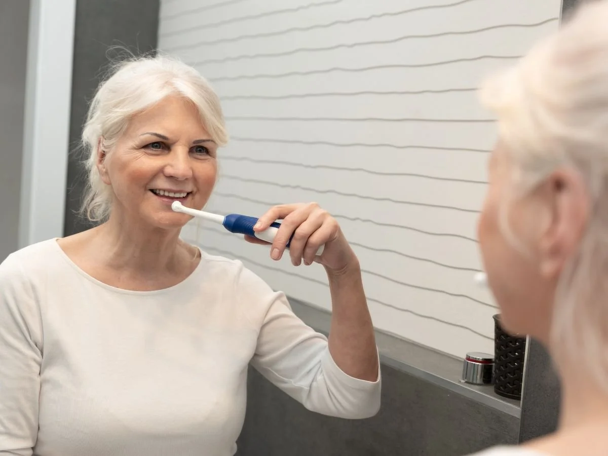 Senior Brushing Teeth In Bathroom Mirror
