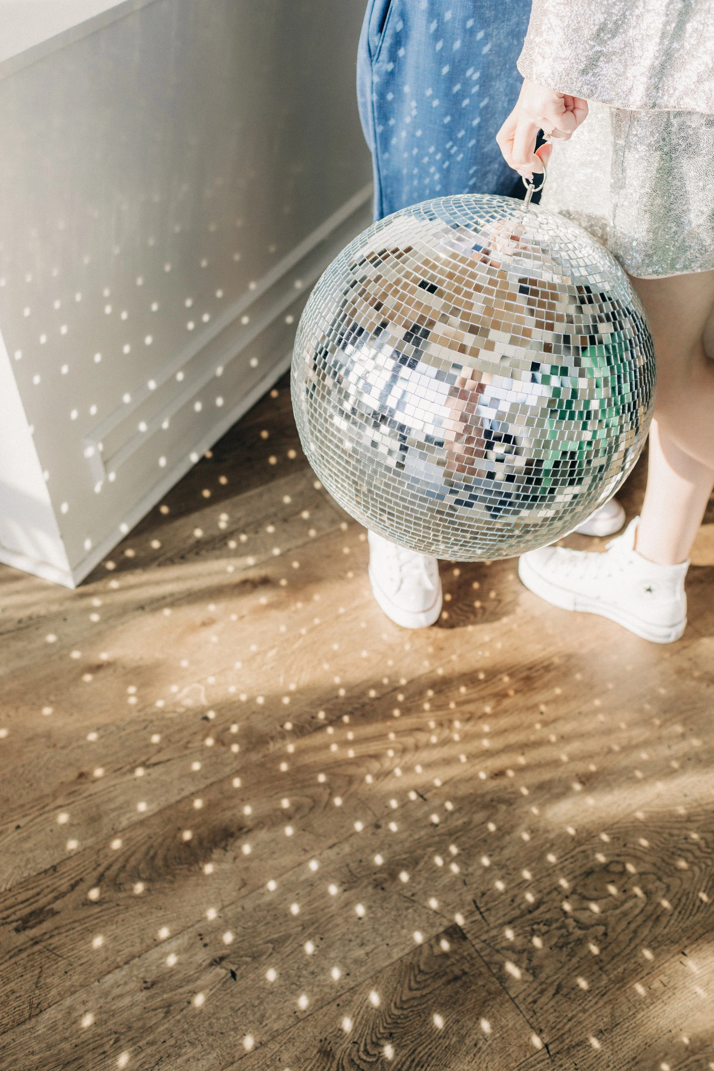 Person holding a disco ball reflecting light on wooden floor