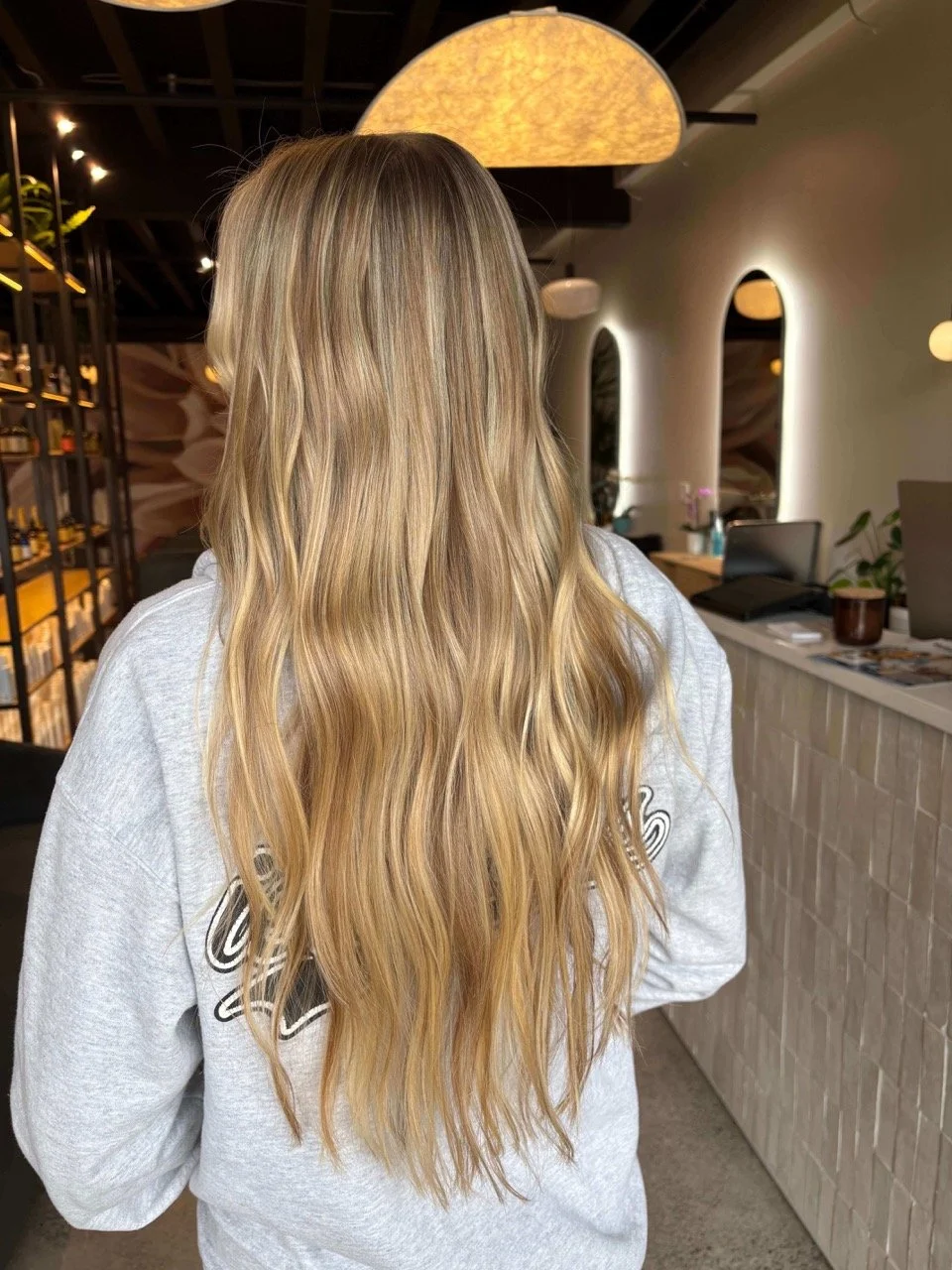 Back of a woman with long, wavy blonde hair inside a modern interior space.