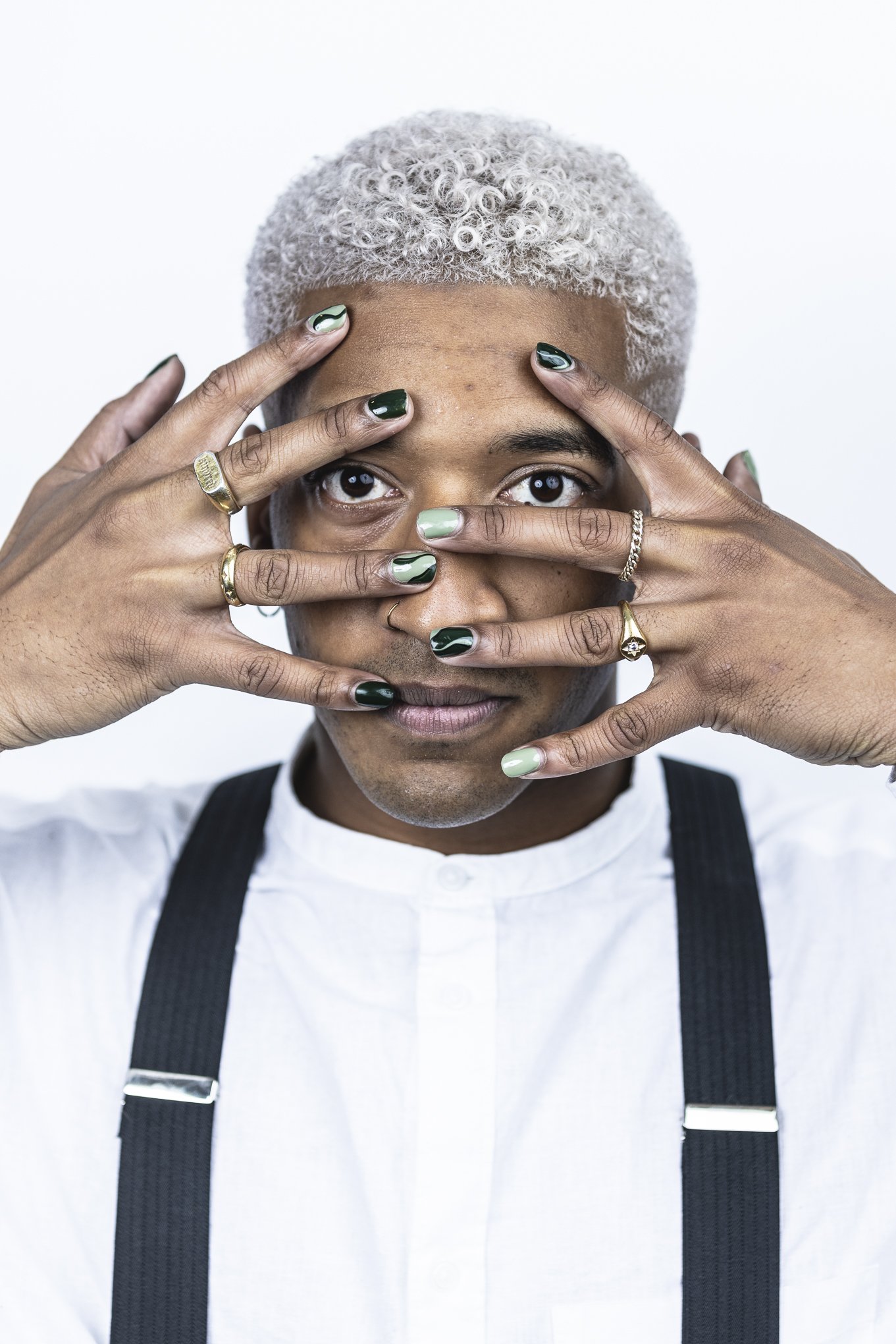 Person with curly gray hair holding hands in front of face, showing green painted nails and wearing rings.