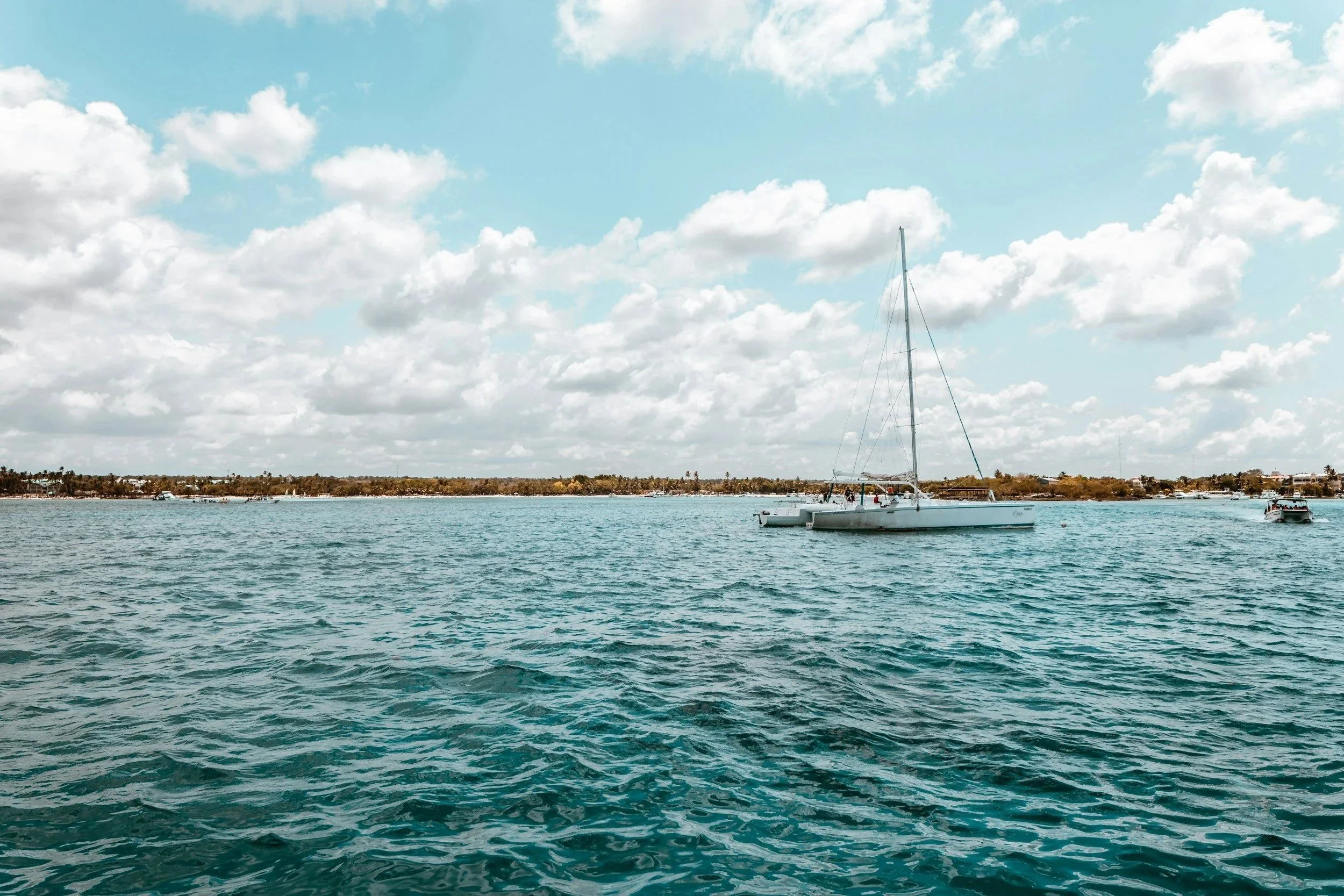 A large white sailboat on a calm body of water under a partly cloudy sky with land visible in the background.