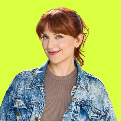 A woman with reddish-brown hair smiling, wearing a denim jacket and a beige shirt, against a bright green background.